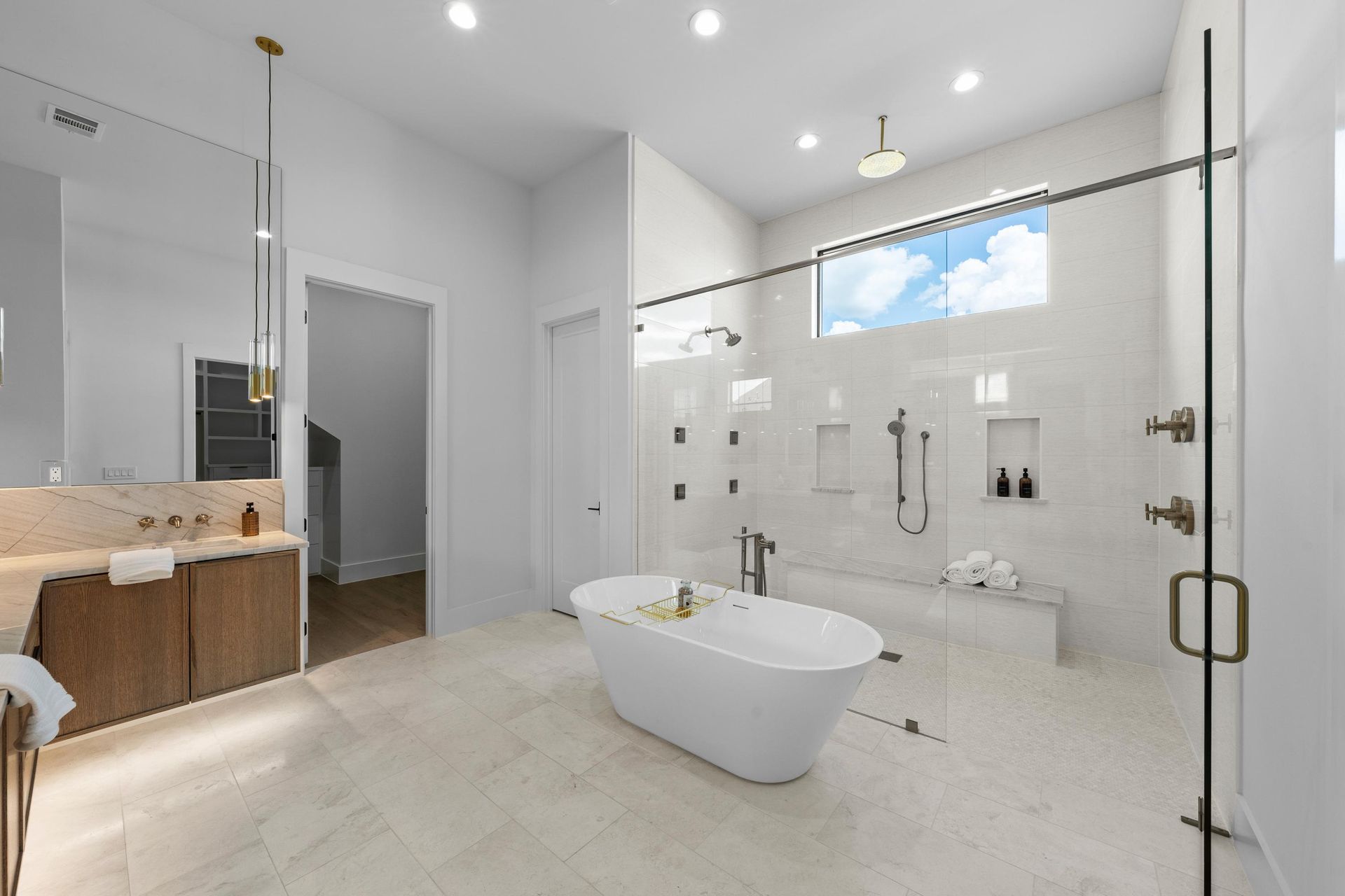 Bright modern bathroom with a freestanding tub, glass shower, vanity, and light tile flooring.