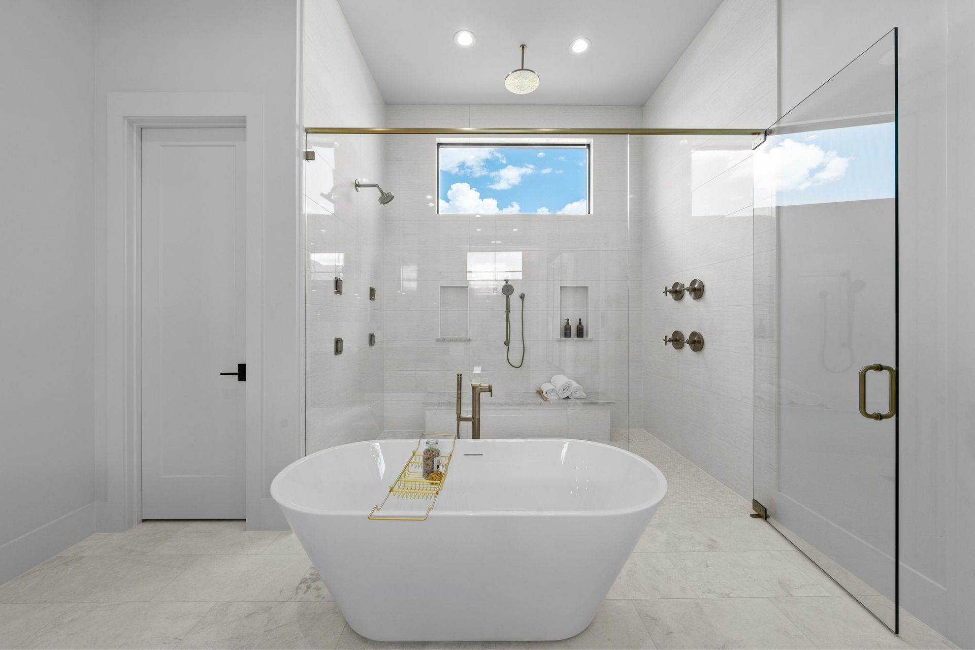 Bright modern bathroom with freestanding tub, glass shower, white tile, and skylight window.