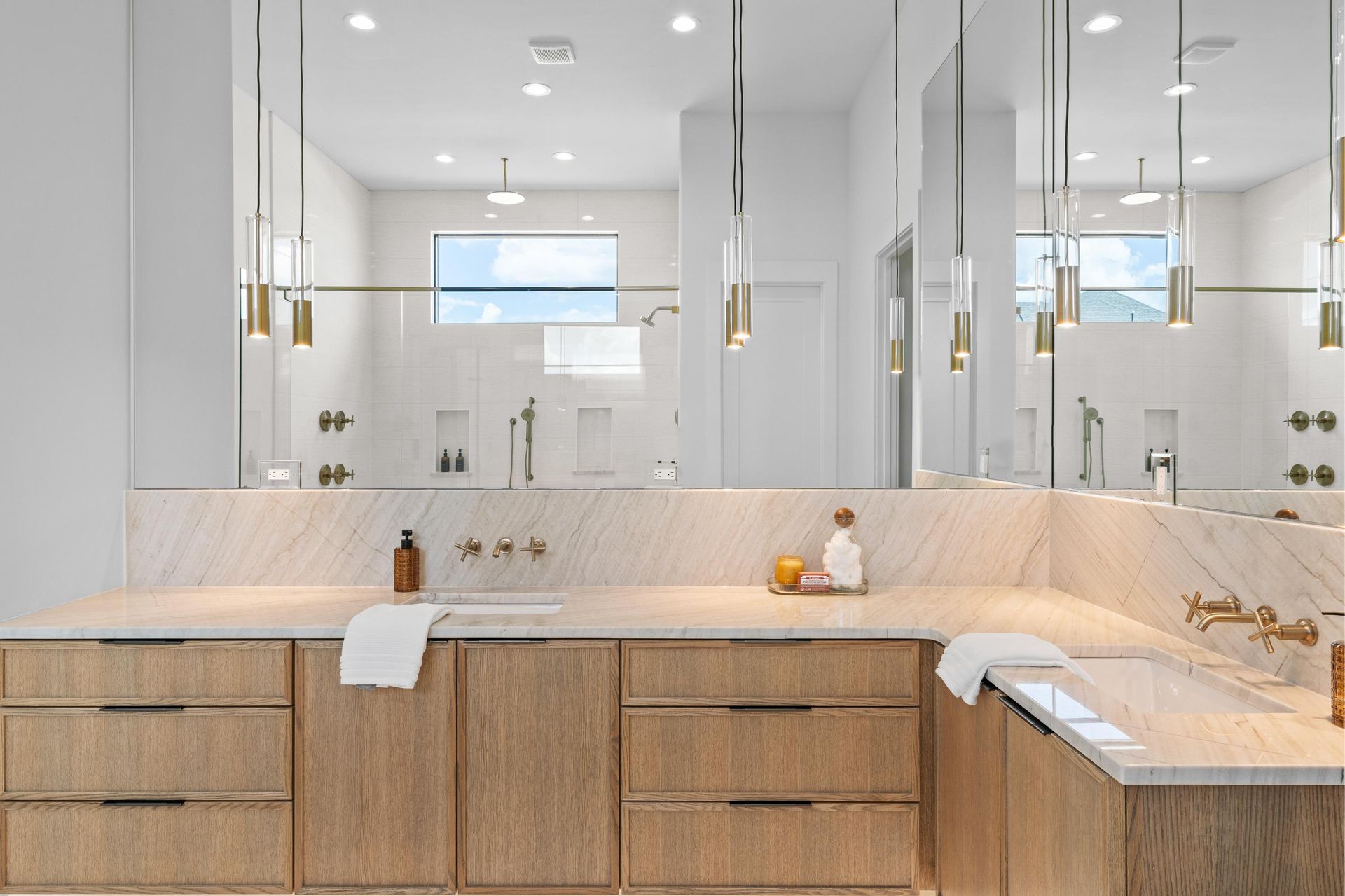 Modern bathroom with double vanity, large mirrors, white counters, and wood cabinetry