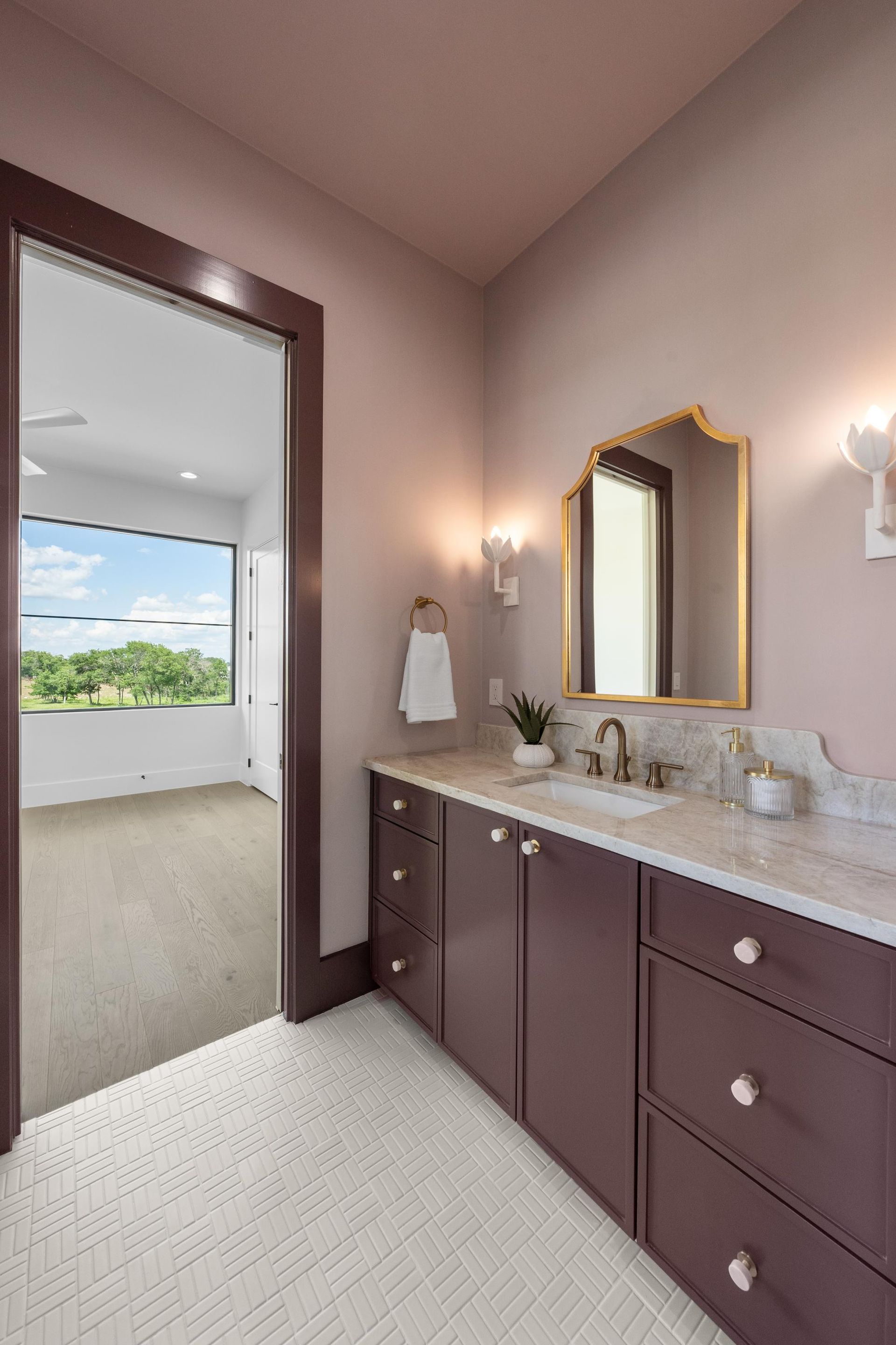 Bathroom vanity with dark cabinets, marble countertop, gold mirror, and open door to a balcony view