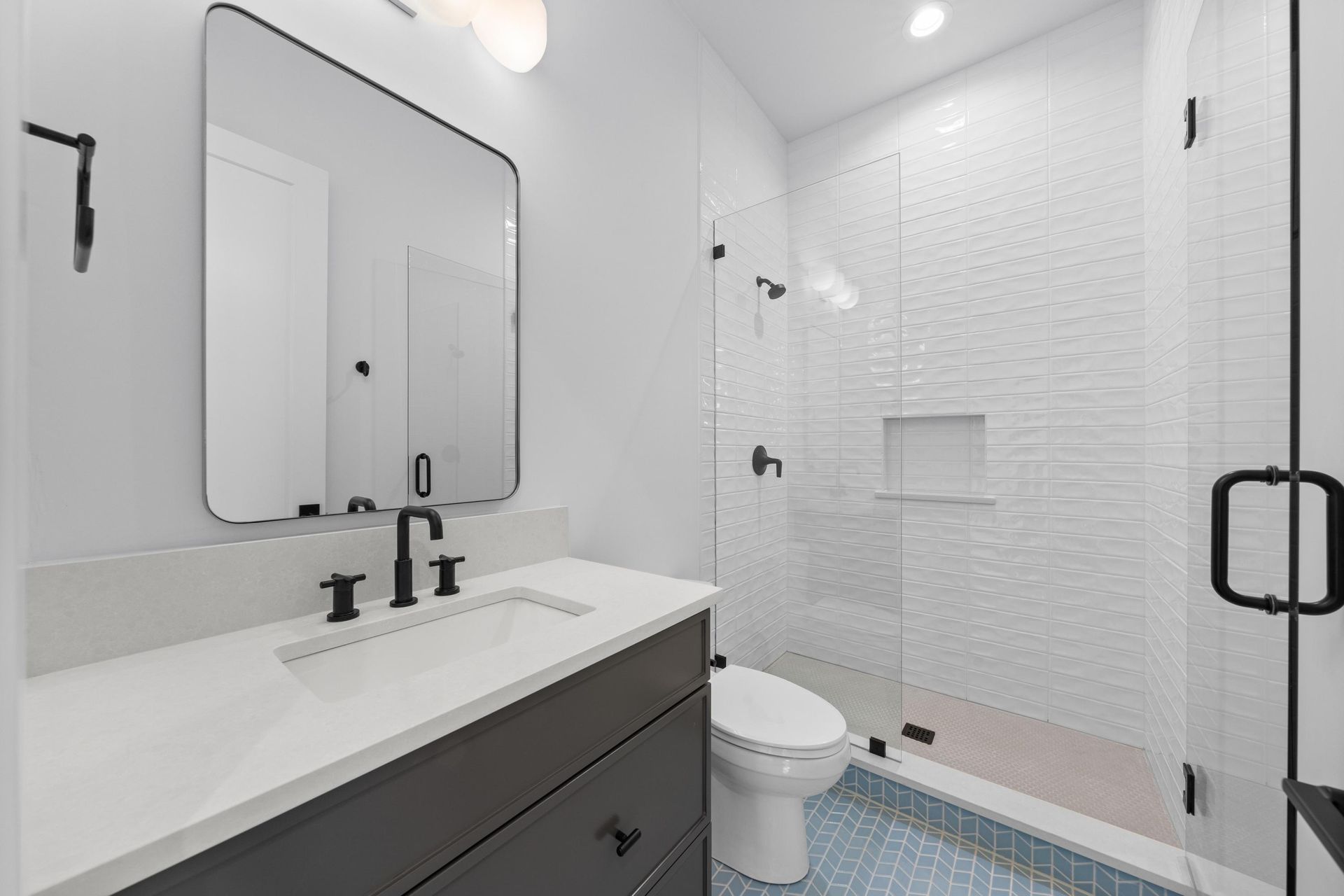 Modern white bathroom with vanity, mirror, toilet, glass shower, and black fixtures