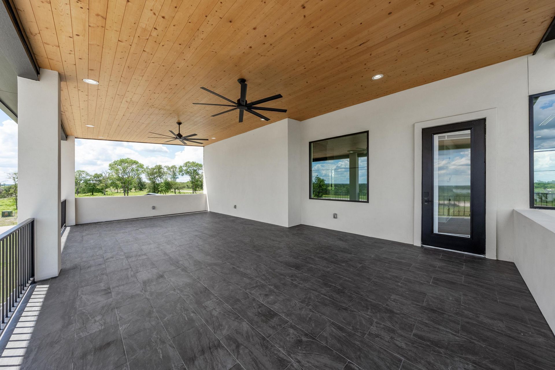 Covered patio with wood ceiling, ceiling fan, and open view of yard through wide openings.