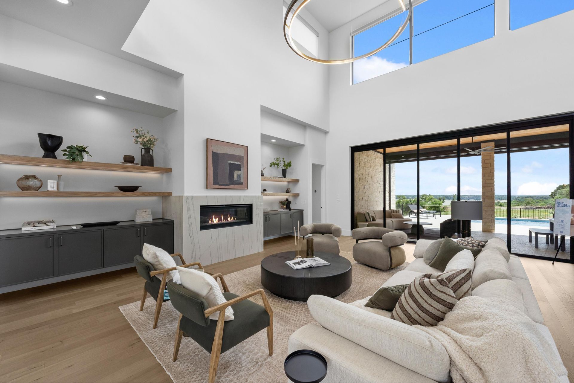 Modern bright living room with beige sofas, fireplace, open kitchen, and large sliding glass doors to a patio.