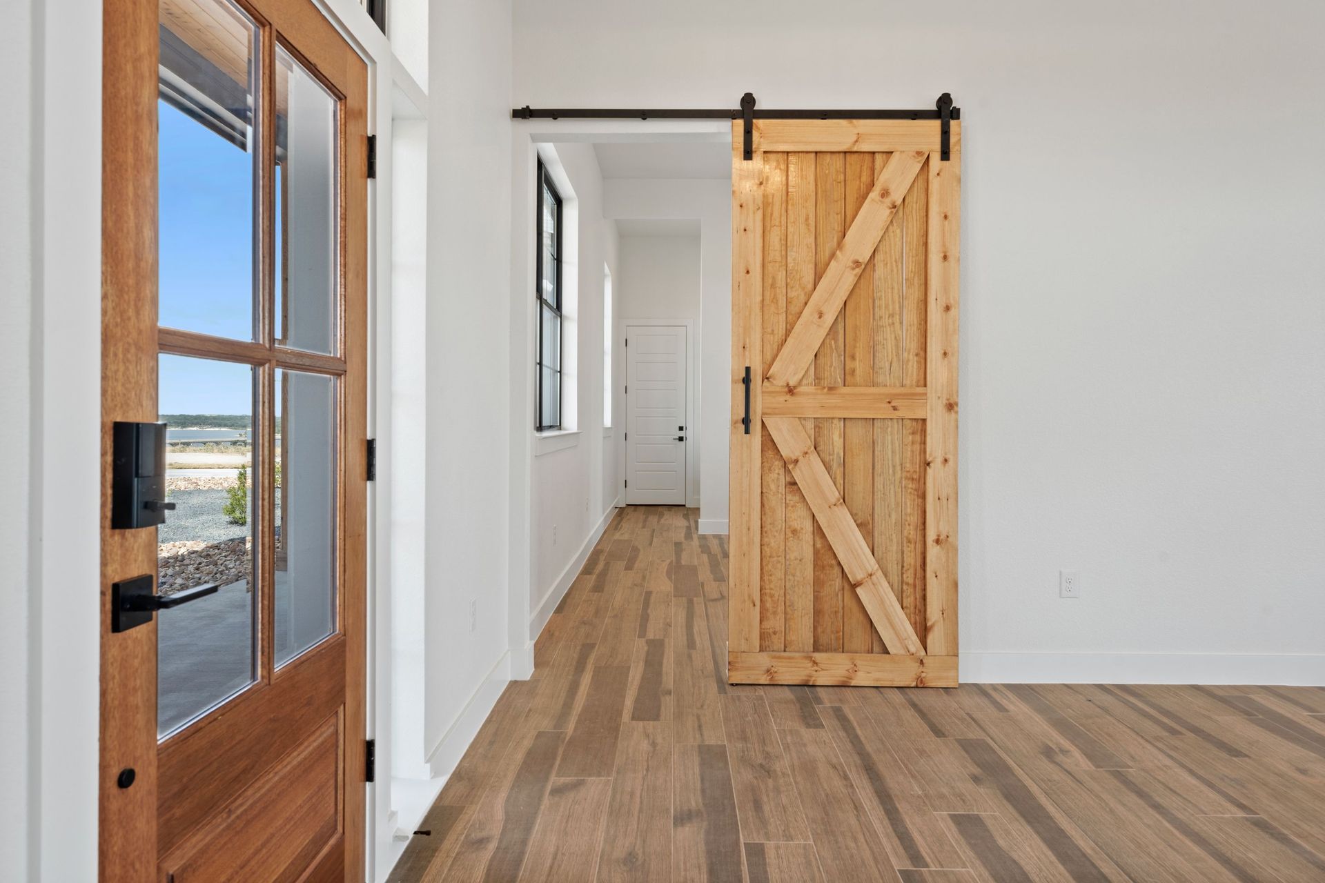Bright hallway with wood floors, white walls, and a rustic sliding barn door leading to a doorway.