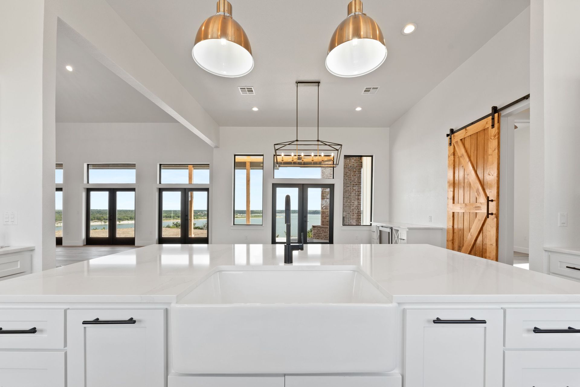 Bright modern kitchen with white cabinets, island, brass pendant lights, and large windows