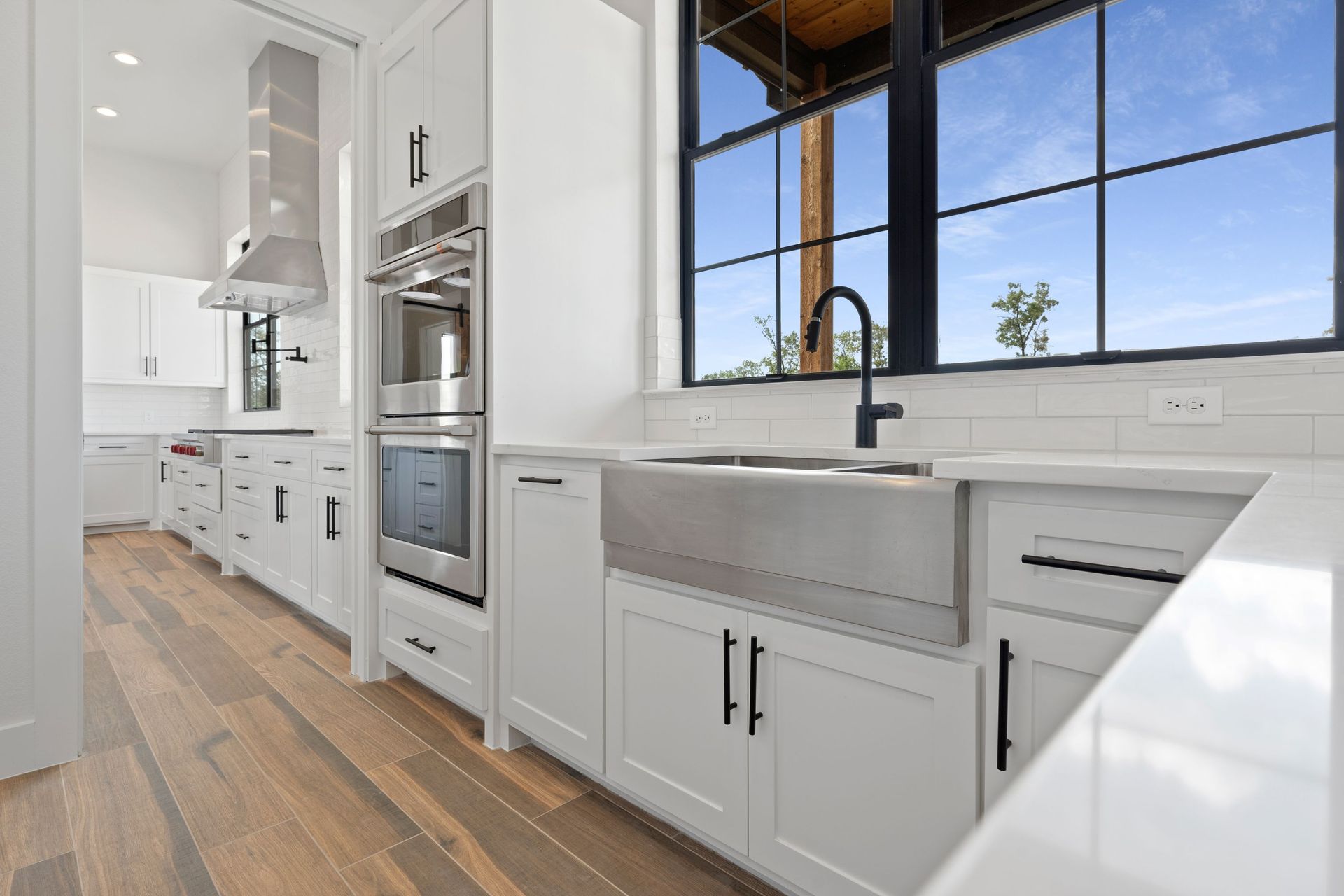 Bright modern white kitchen with island, built-in oven, large windows, and wood floors
