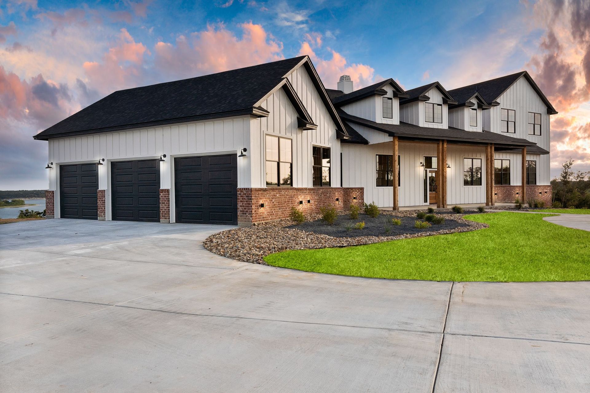 Modern two-story suburban house with a three-car garage, stone accents, and a manicured lawn at sunset