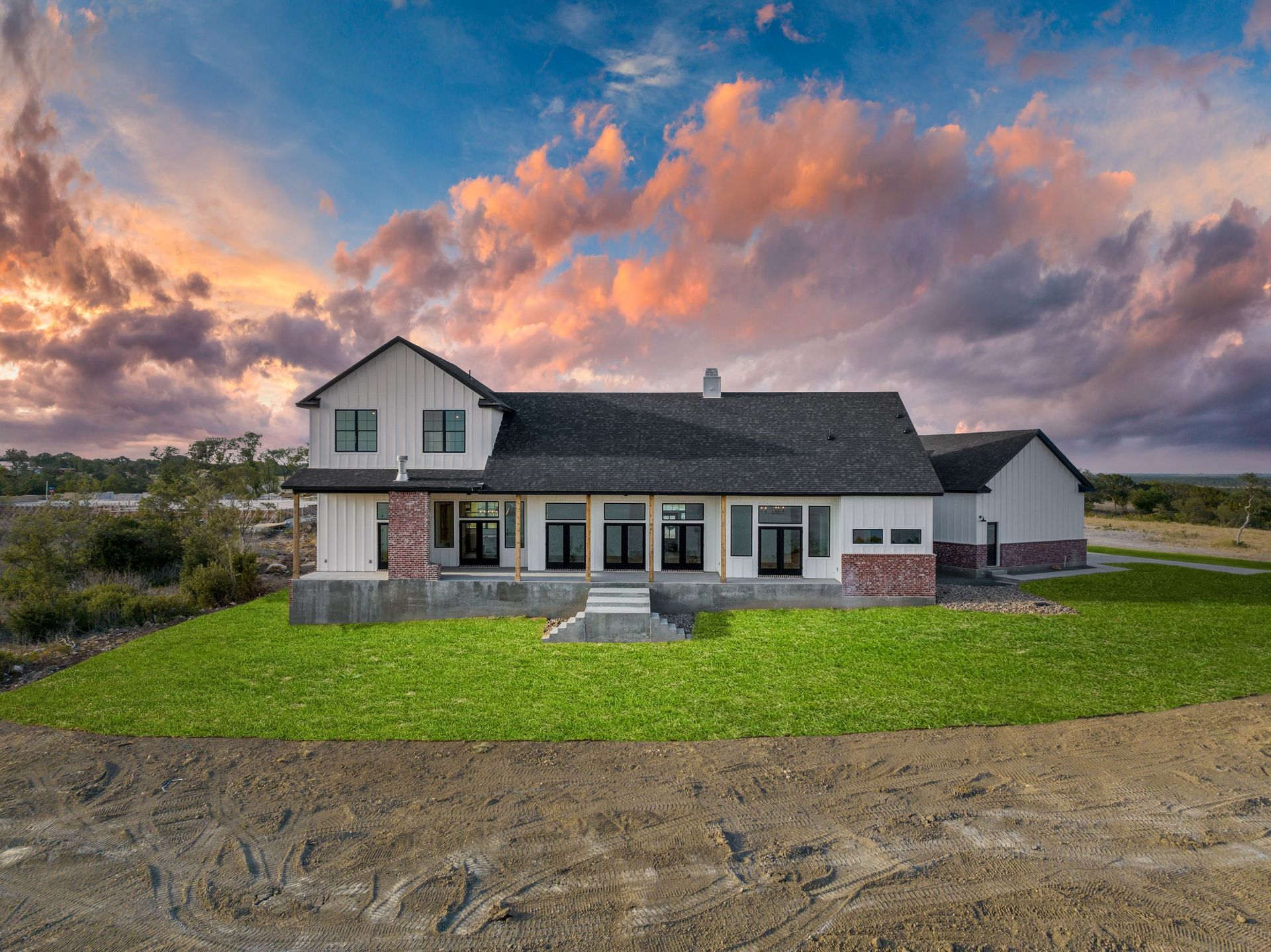 Single-story house with gray roof and green lawn under a dramatic sunset sky