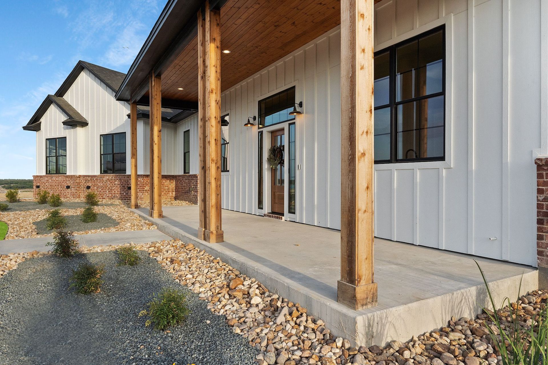 Modern farmhouse-style house exterior with white siding, porch posts, and gravel landscaping