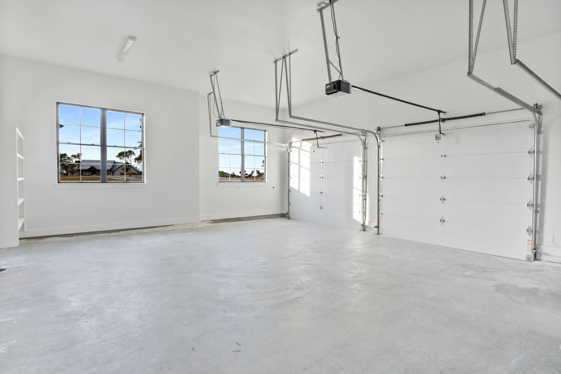 Empty white garage interior with concrete floor, windows, and closed overhead door