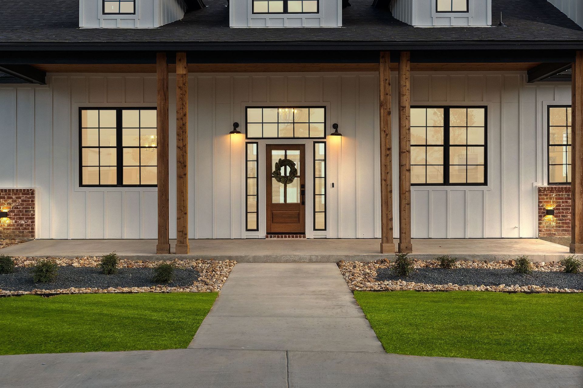 Modern house front entry with lit sconces, white siding, dark roof, and a central walkway leading to the porch