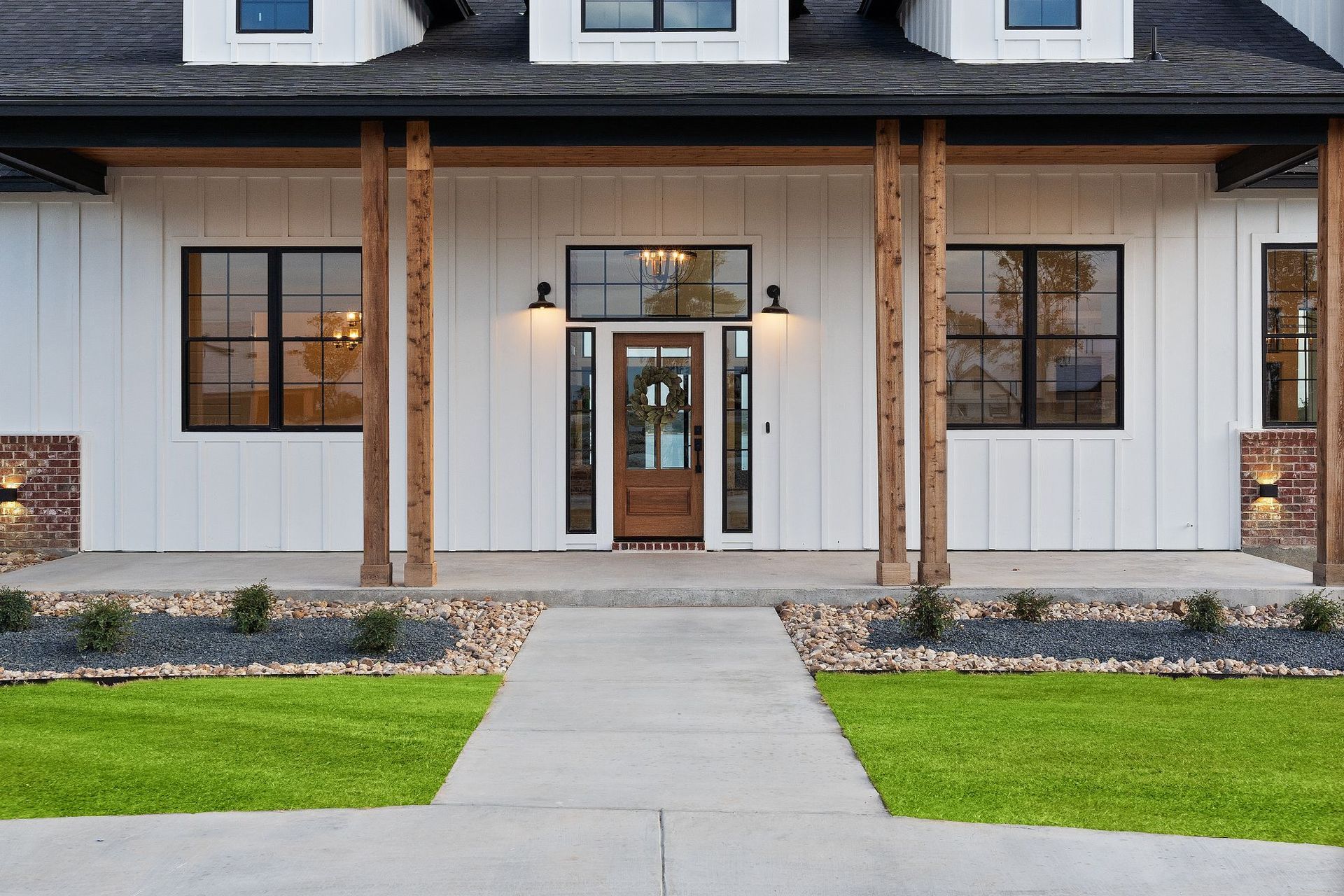 Front view of a modern white house with a centered porch, black roof, and green lawn.