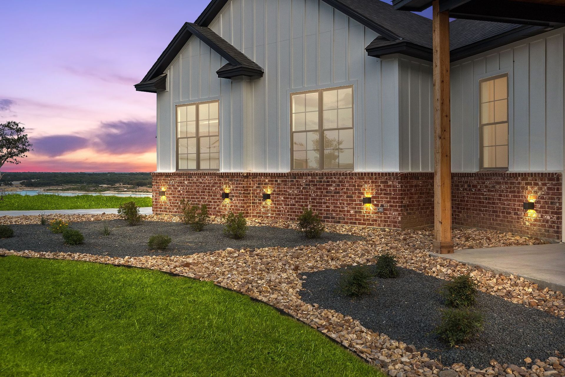 House exterior with lit stone facade, landscaped yard, and a sunset sky