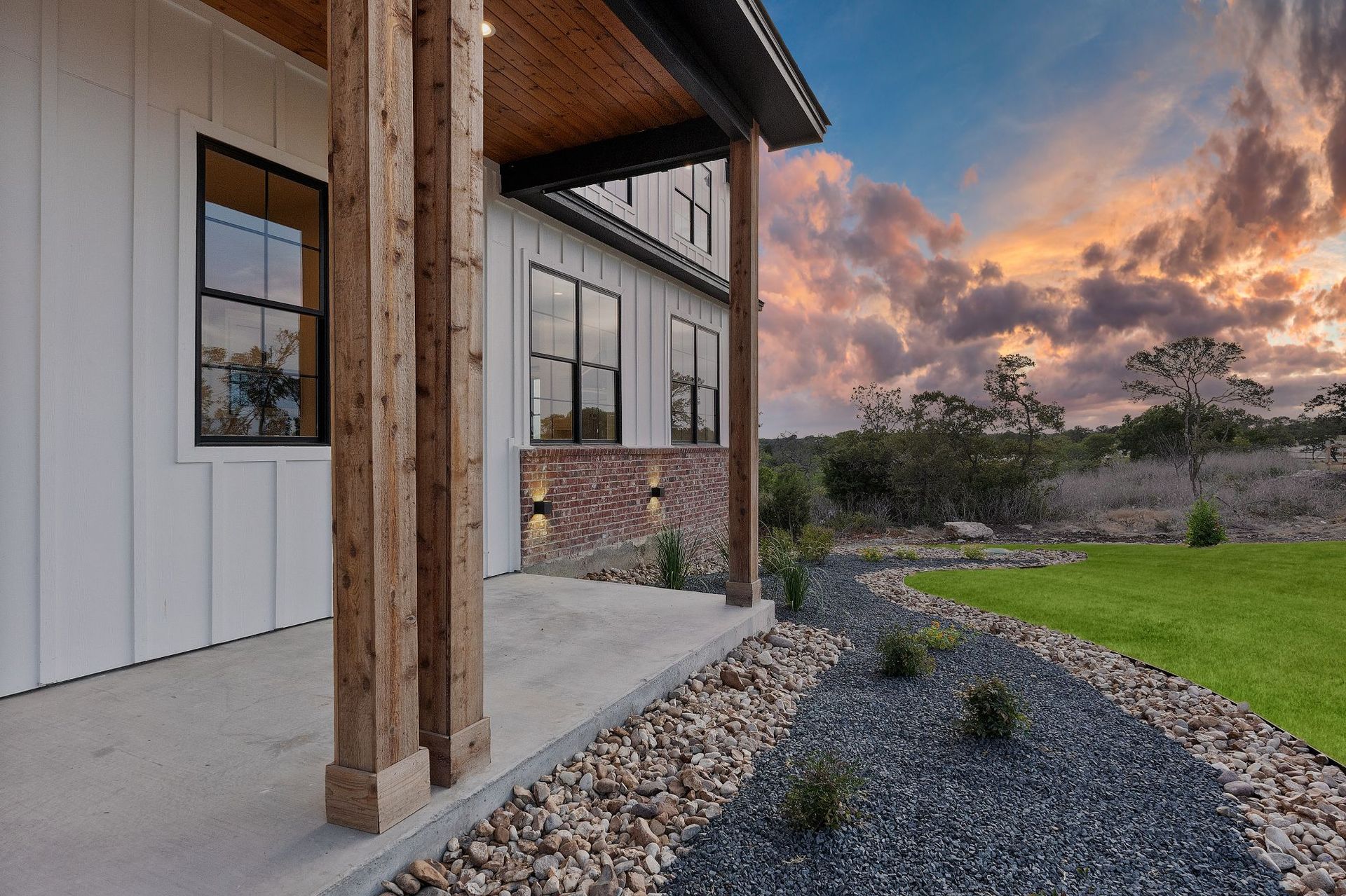 Modern house exterior with wood posts, stone accents, gravel landscaping, and a sunset sky