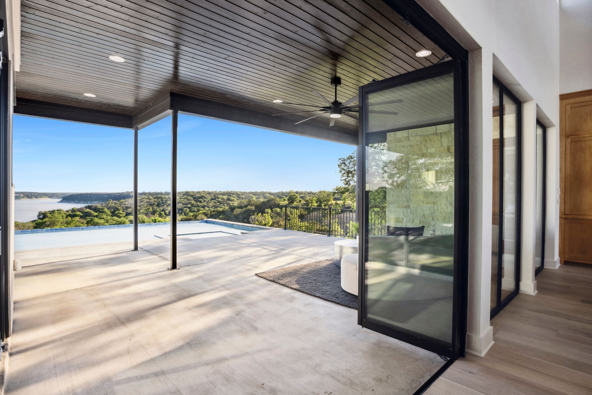 Modern patio with open glass doors, pool, and panoramic water and hillside view
