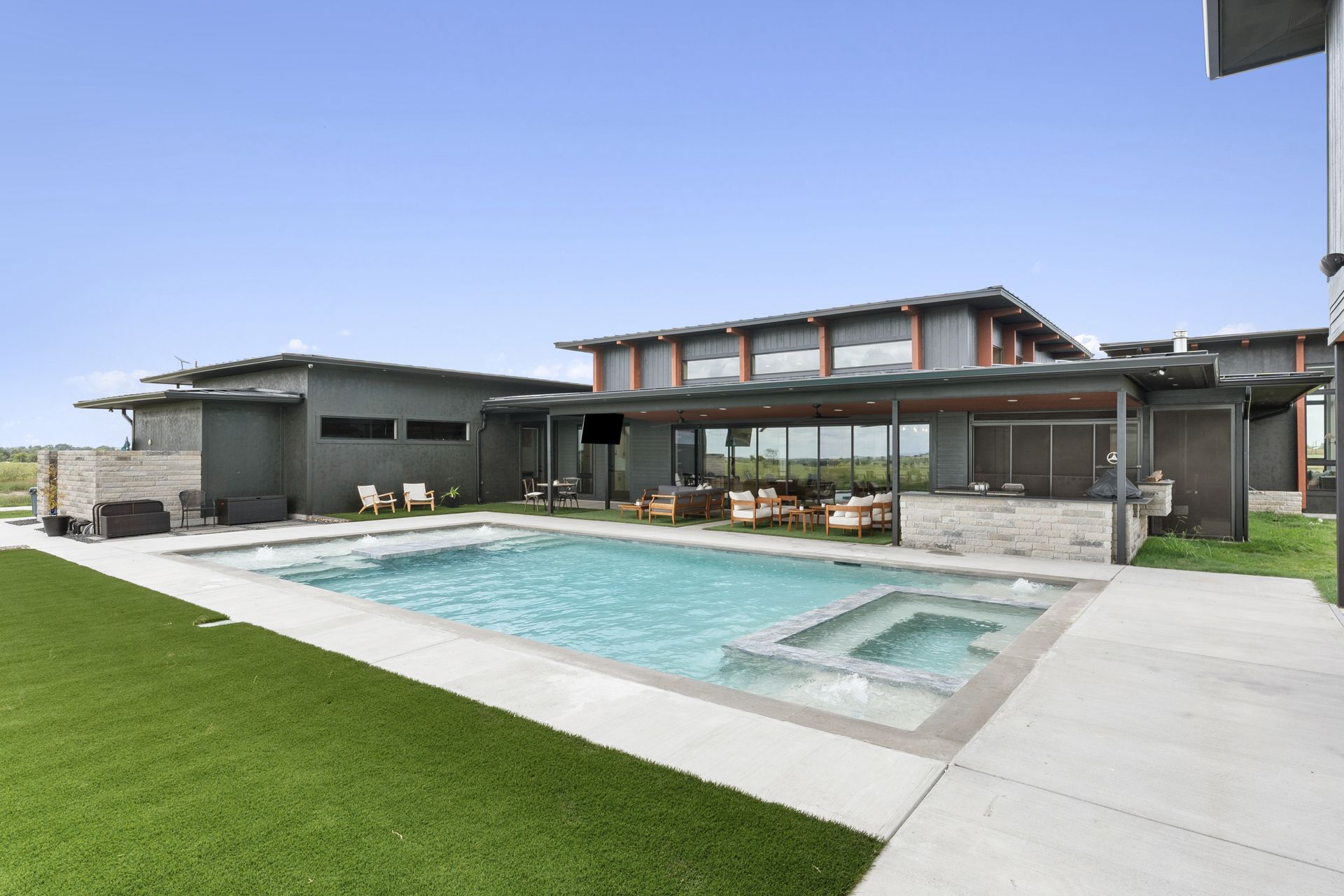 Modern house with a large backyard pool, spa, and green lawn under a clear sky