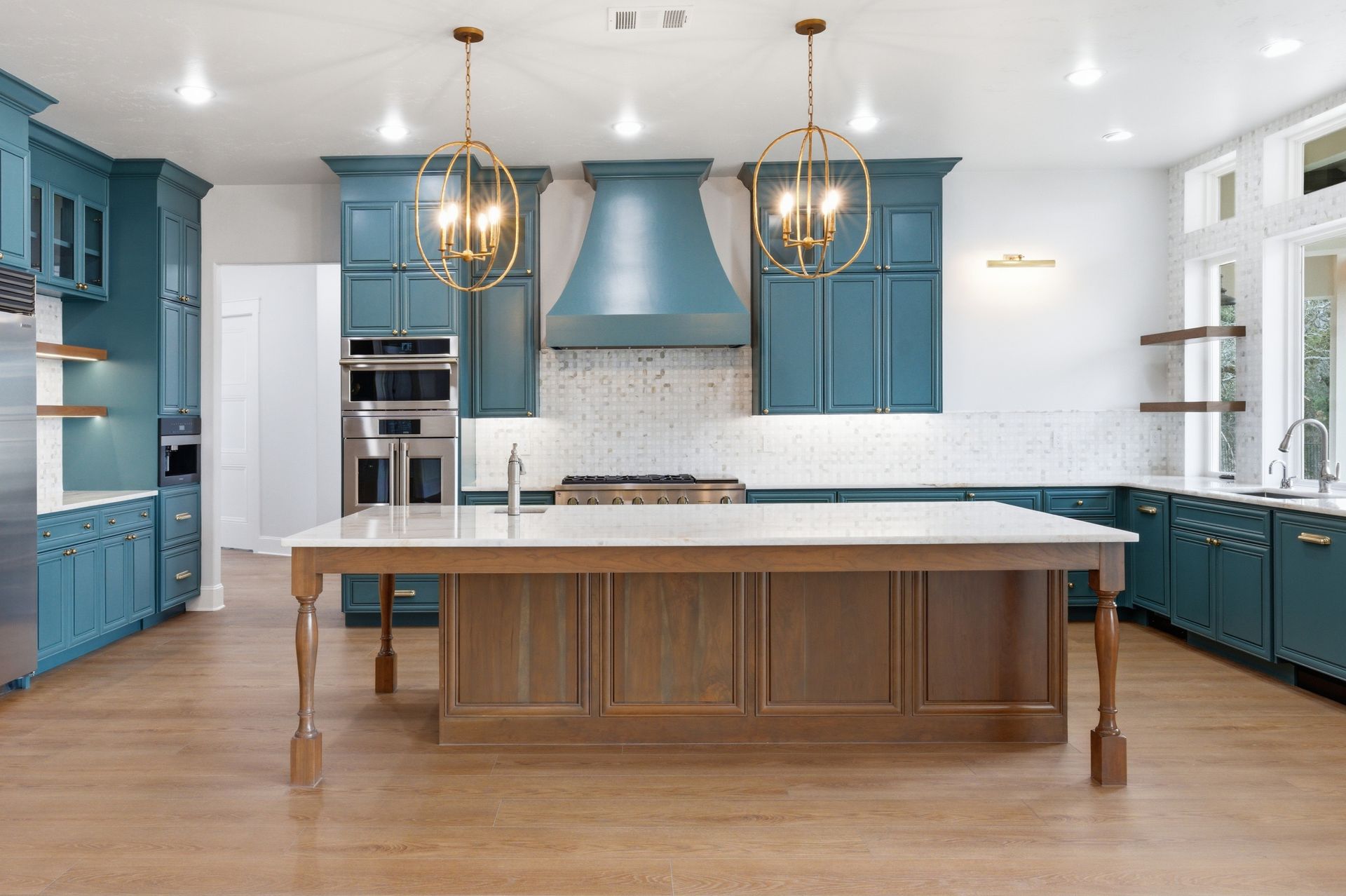 Spacious modern kitchen with blue cabinets, white island, wood floors, and brass pendant lights