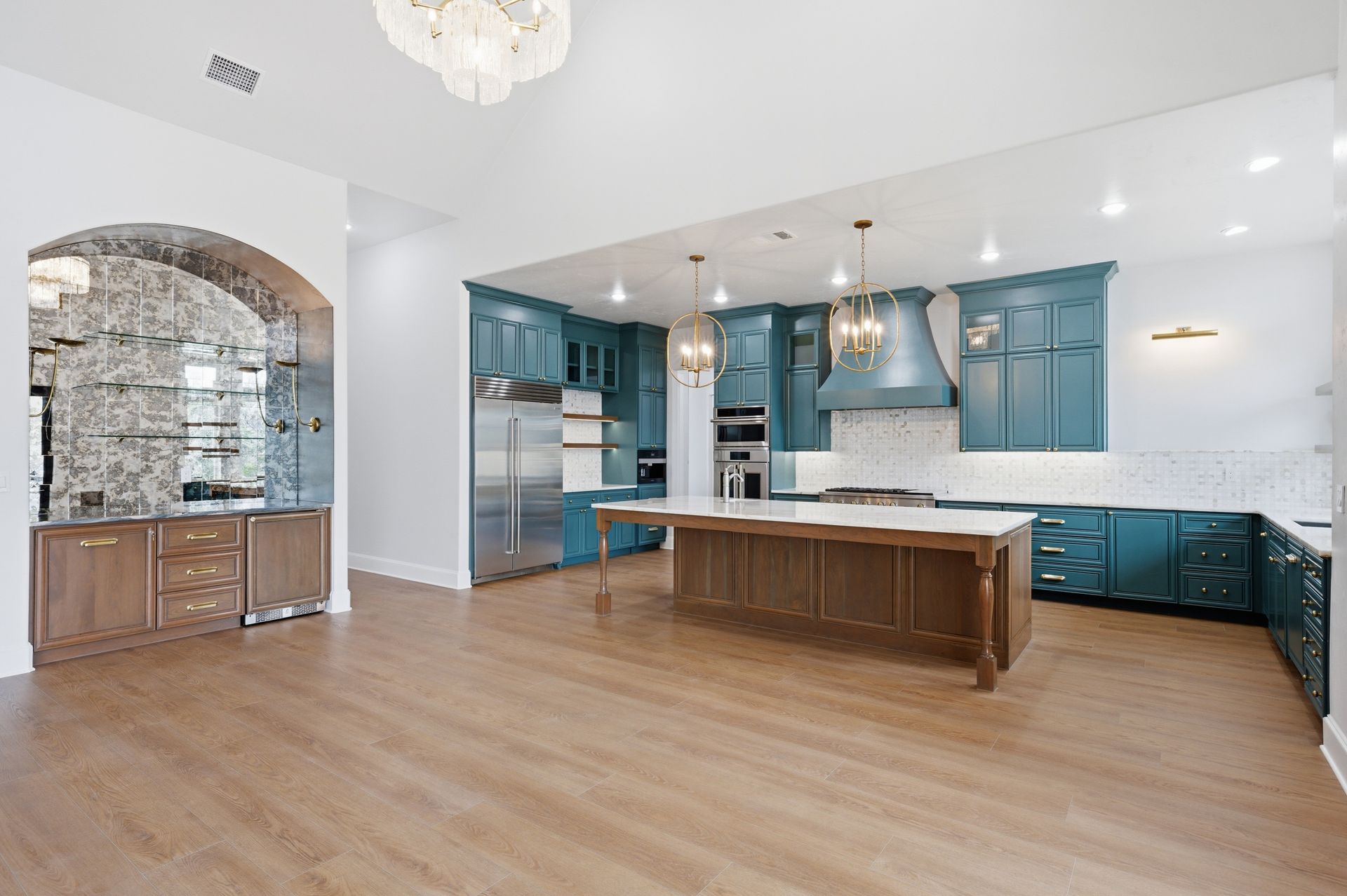 Bright kitchen with blue cabinets, large island, wood floors, and arched stone alcove