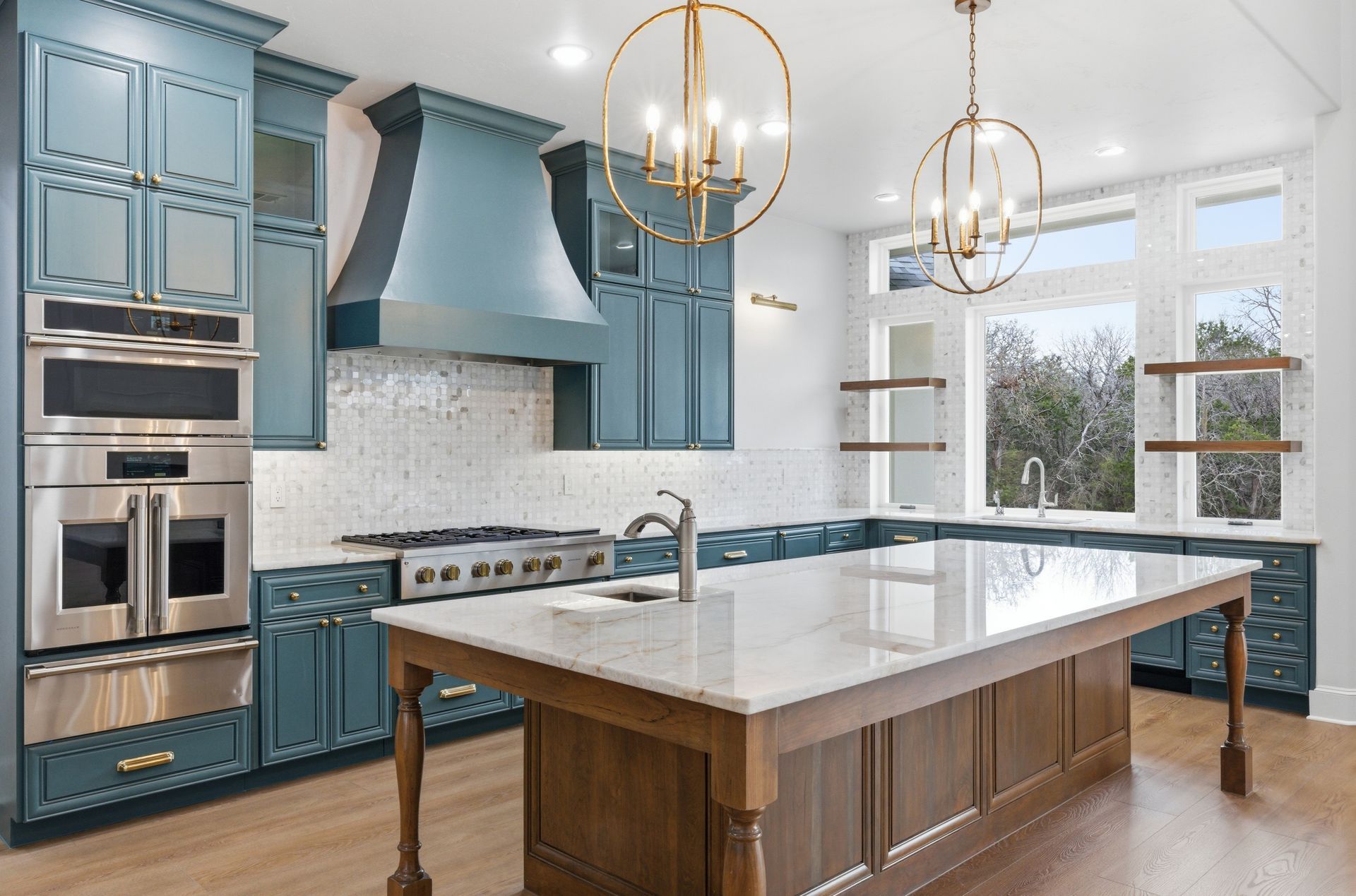 Bright modern kitchen with blue cabinets, white island, stainless appliances, and gold pendant lights