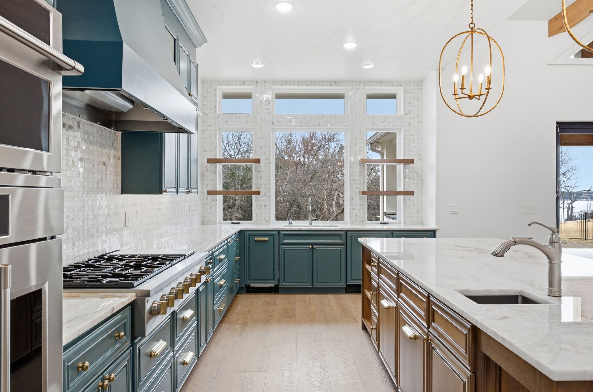 Bright modern kitchen with blue cabinets, large windows, and a white island with sink.