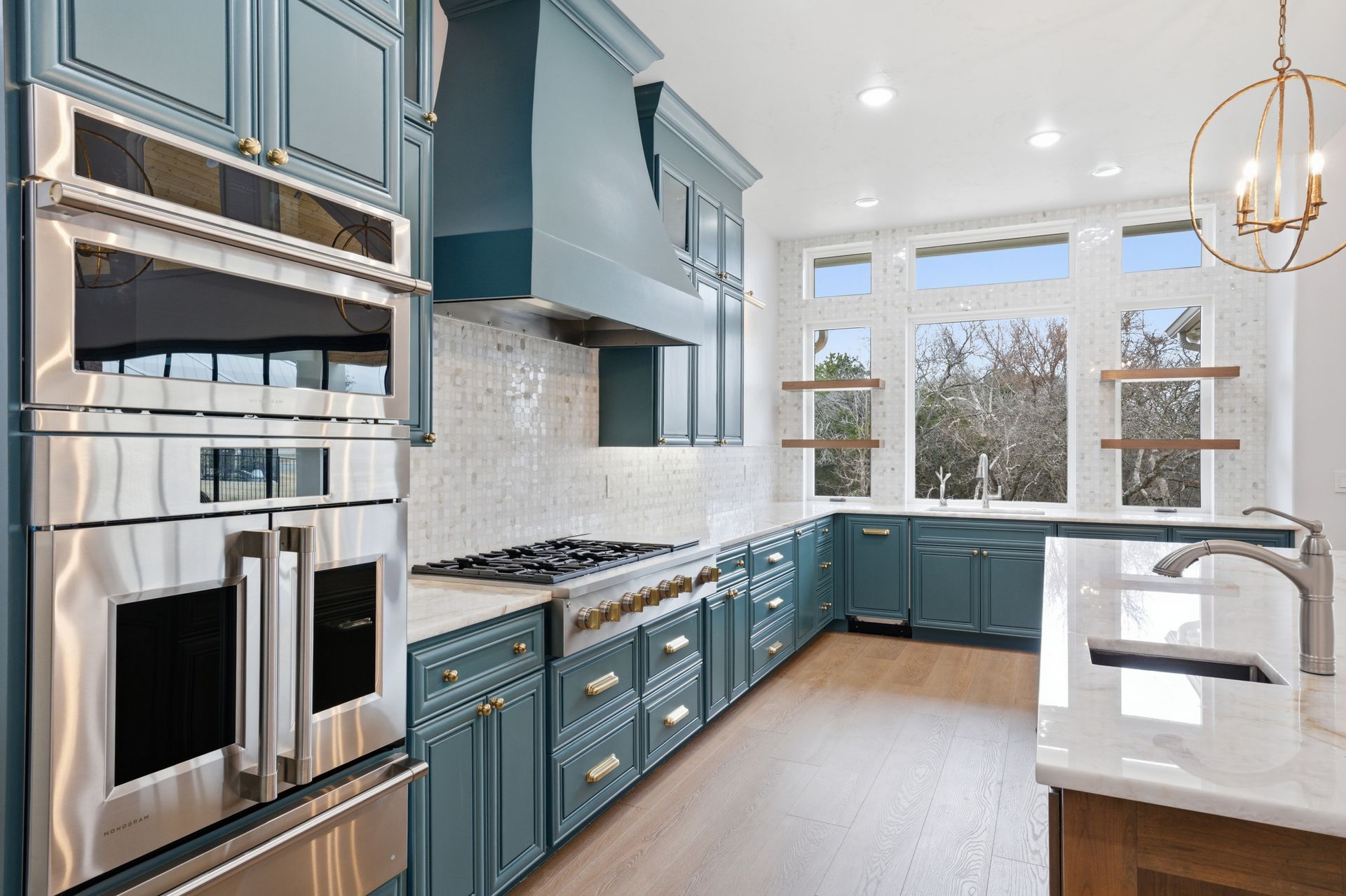 Bright modern kitchen with blue cabinets, stainless steel appliances, and a large window over the sink