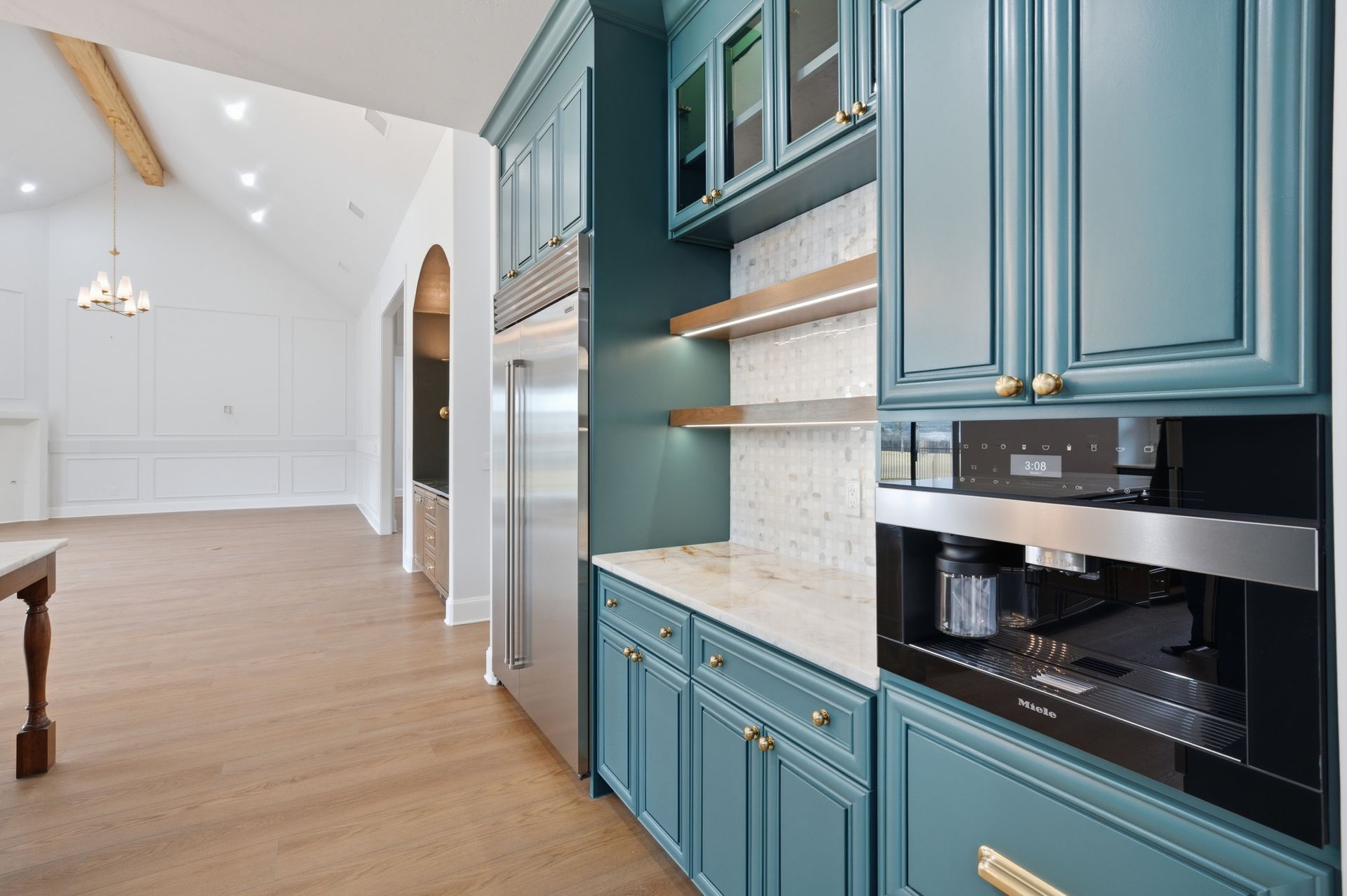 Bright open kitchen with teal cabinets, built-in oven, and light wood floors leading to a white dining area.