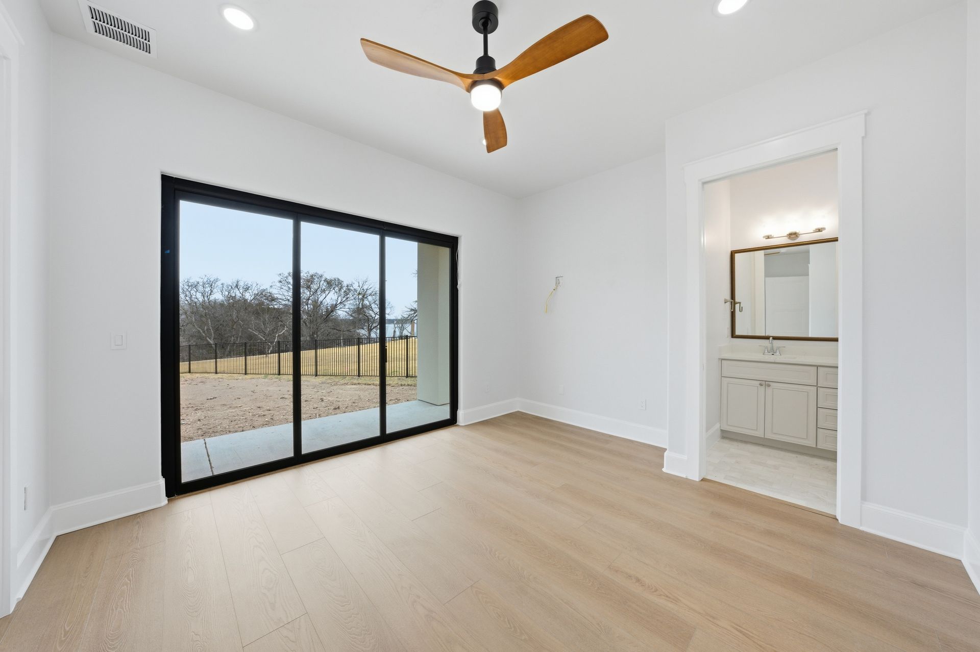 Bright empty bedroom with white walls, wood floors, ceiling fan, and sliding glass doors to a patio.