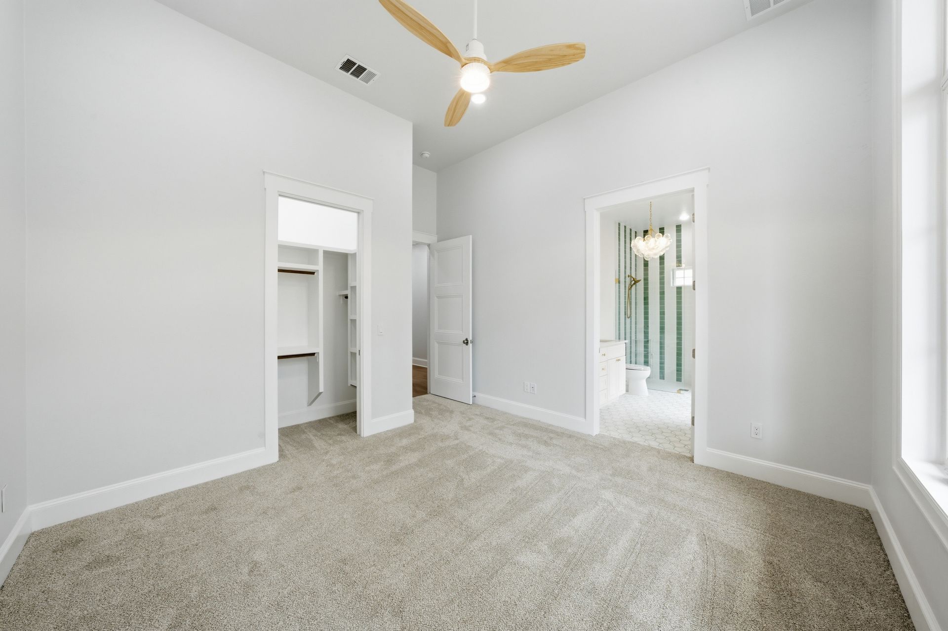 Empty white carpeted bedroom with ceiling fan and walk-in closet openings