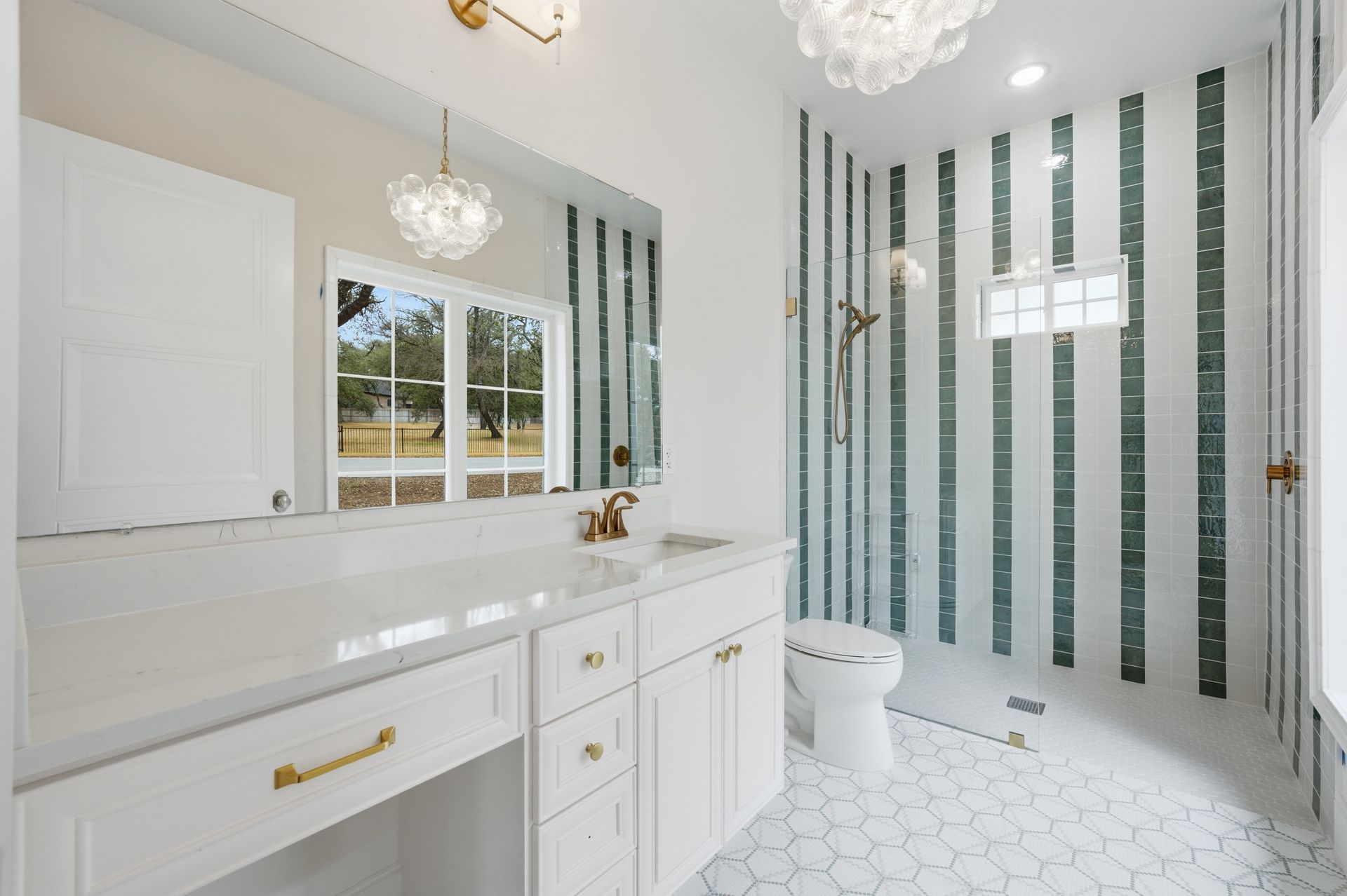Bright white bathroom with gold fixtures, striped tile shower wall, vanity, and toilet