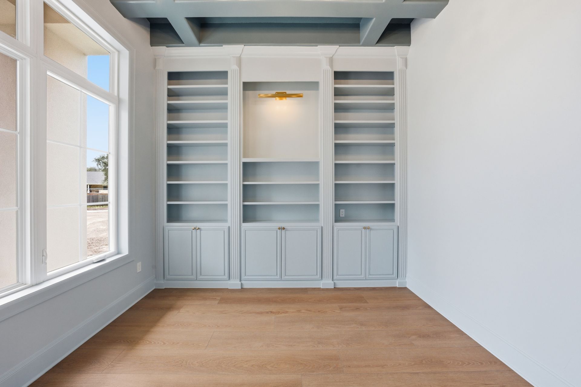 Empty white built-in shelving and cabinets in a bright room with wood floors.