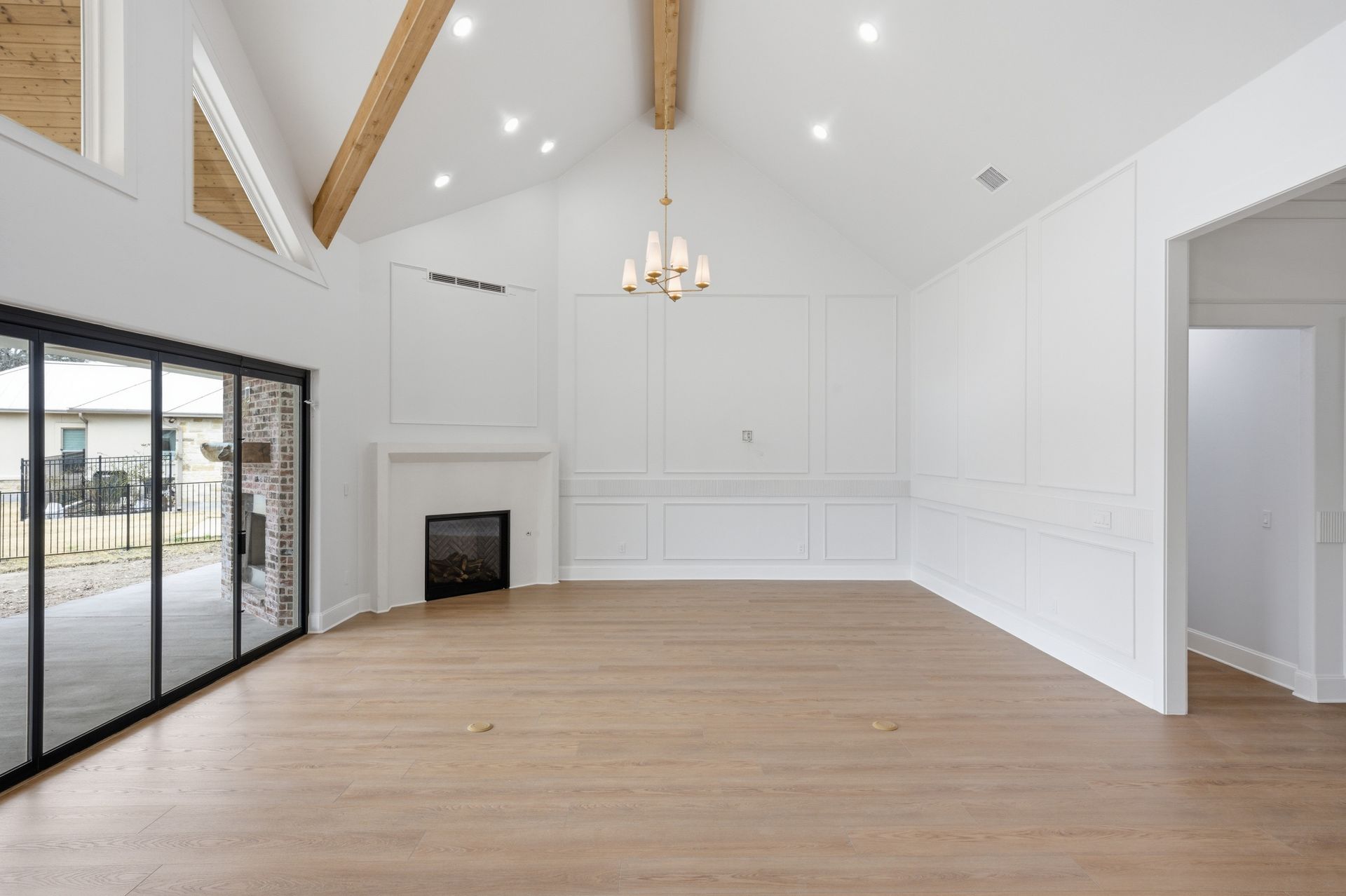 Bright empty living room with vaulted ceiling, white walls, fireplace, hardwood floor, and sliding glass doors