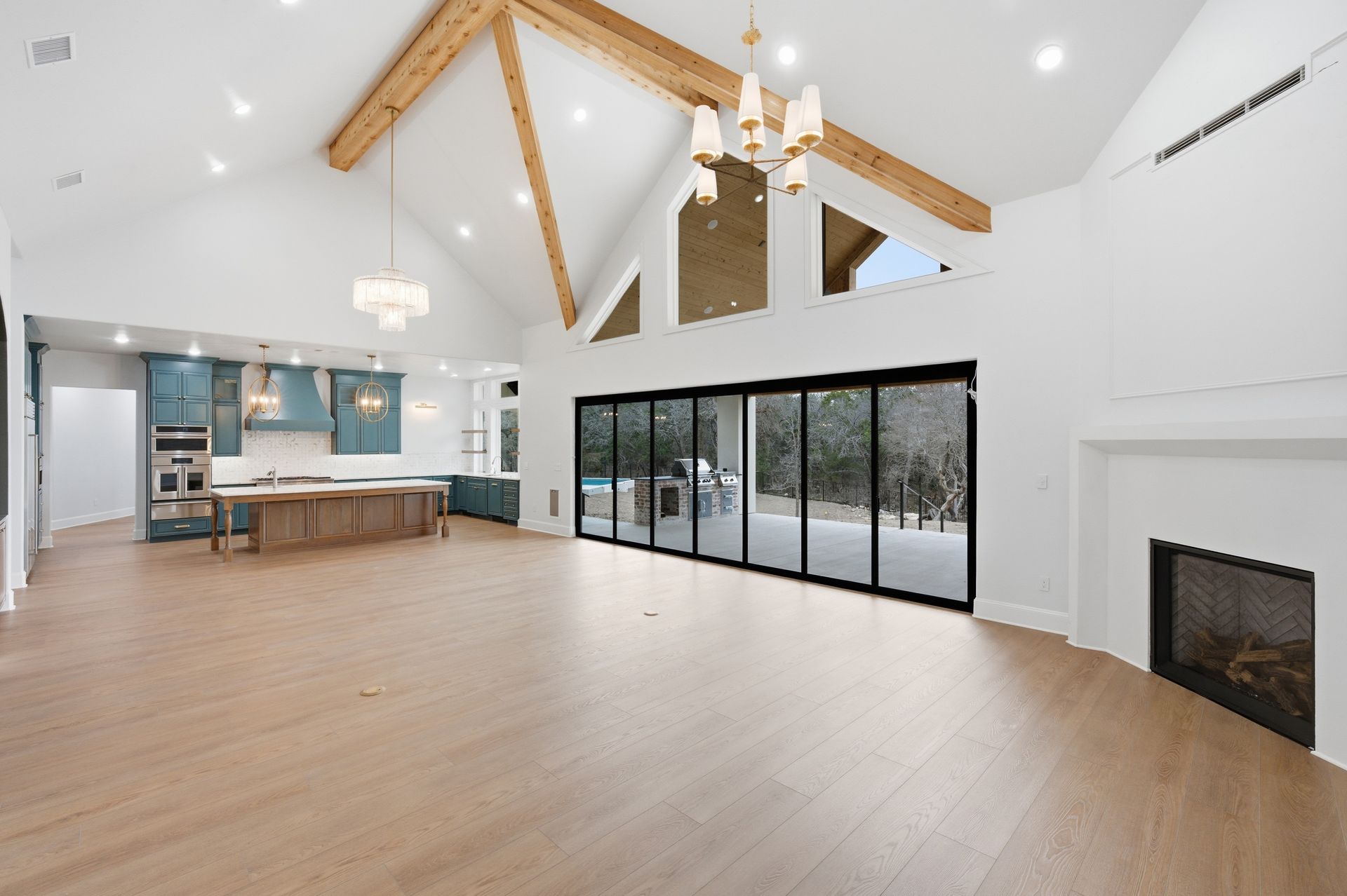 Bright open living room with vaulted wood beams, kitchen island, large glass doors, and fireplace