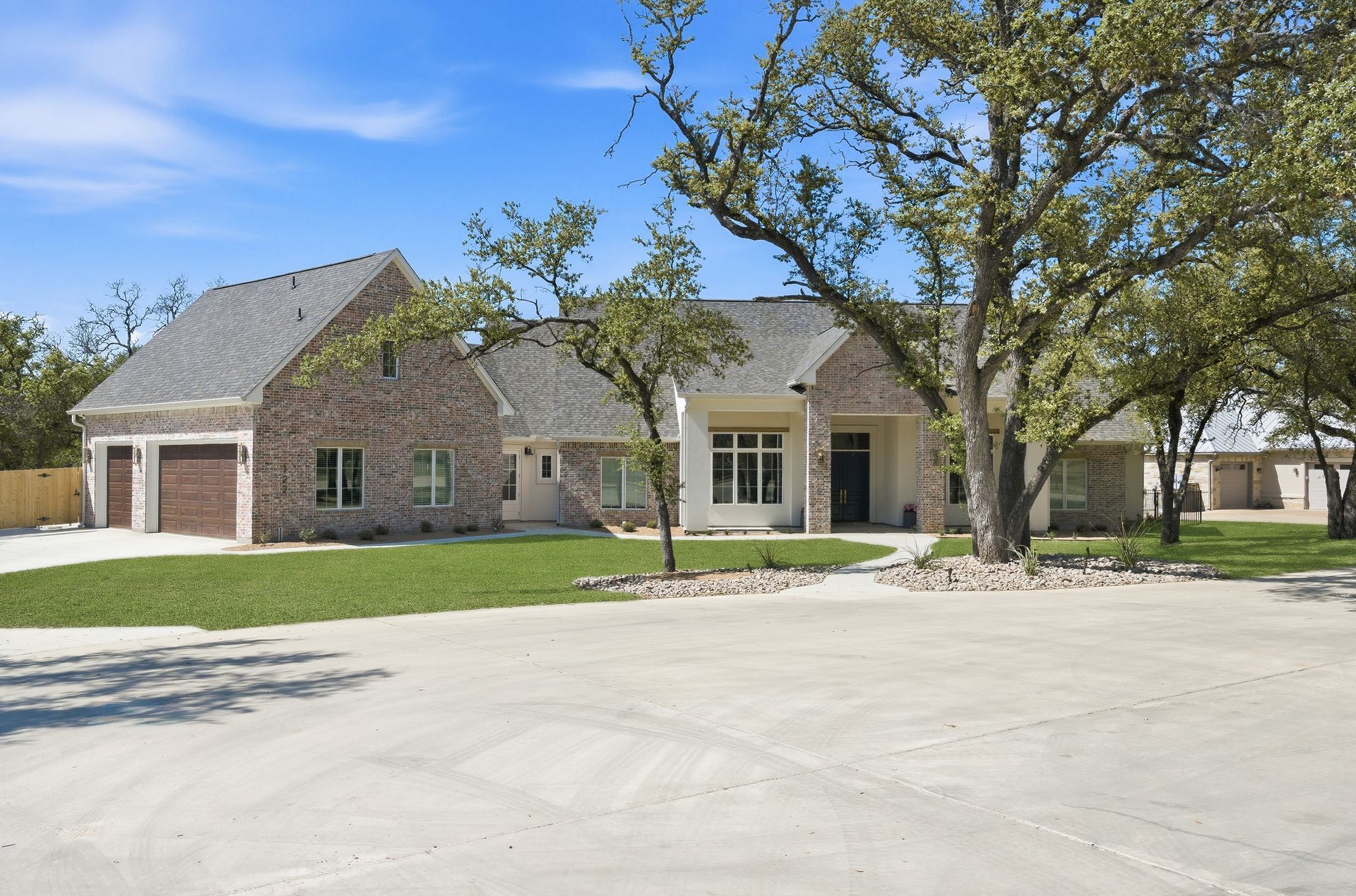 Suburban brick house with a large front yard, driveway, and trees under a clear sky