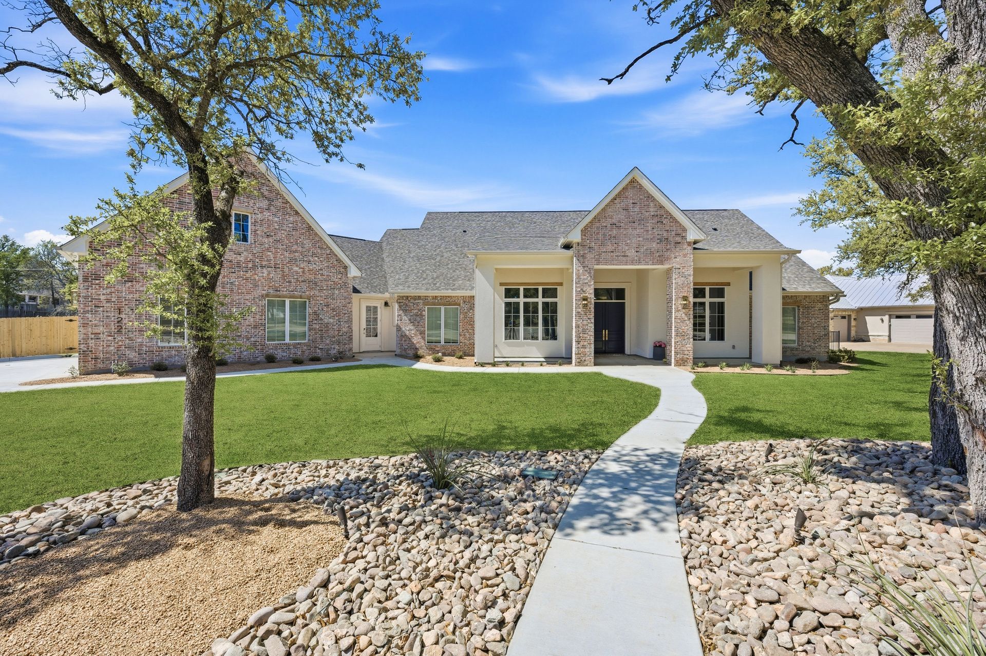 Stone suburban house with a manicured lawn, rock landscaping, and a curved walkway under a blue sky