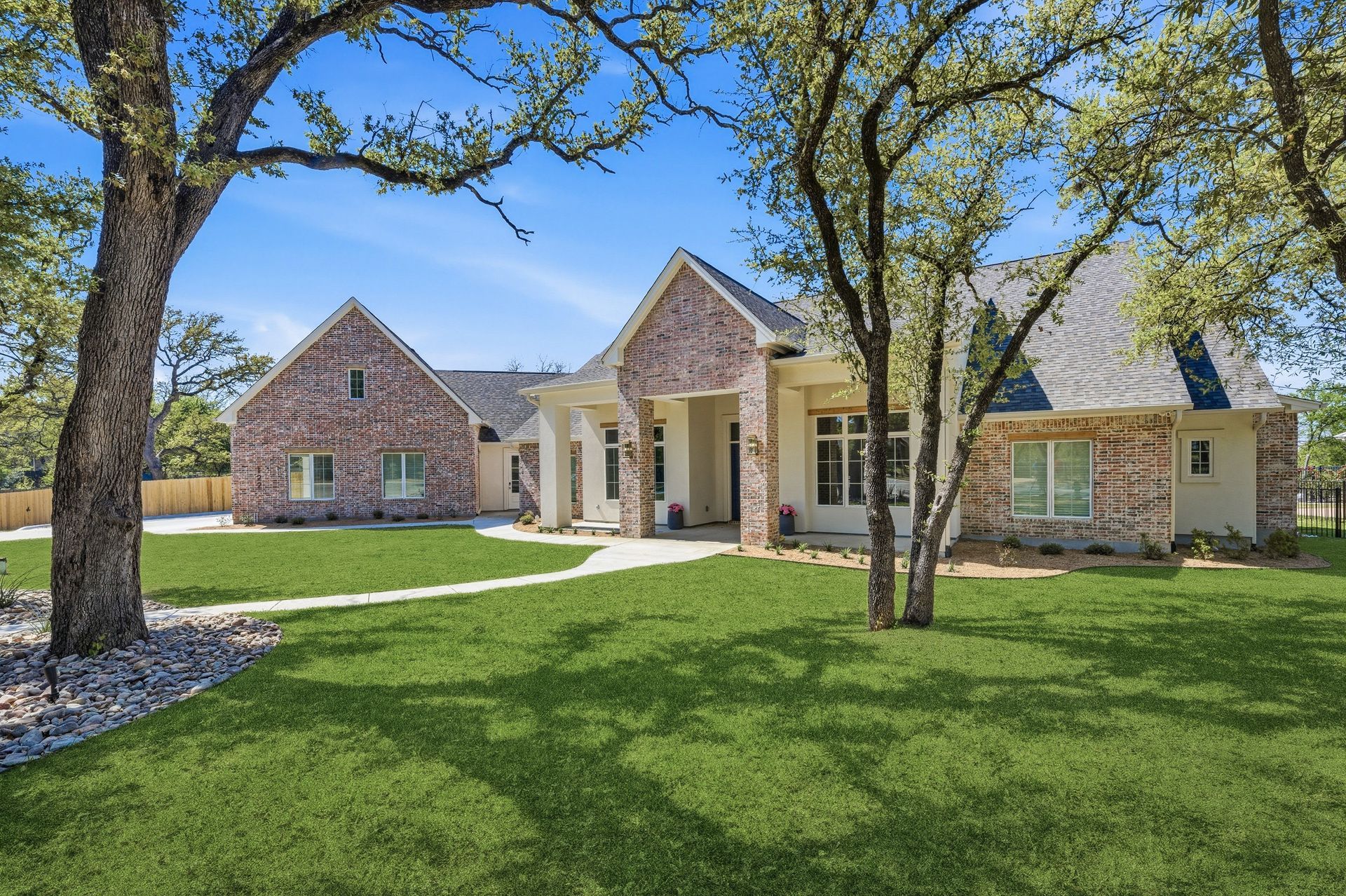 Brick suburban house with columns, green lawn, and trees under a clear blue sky