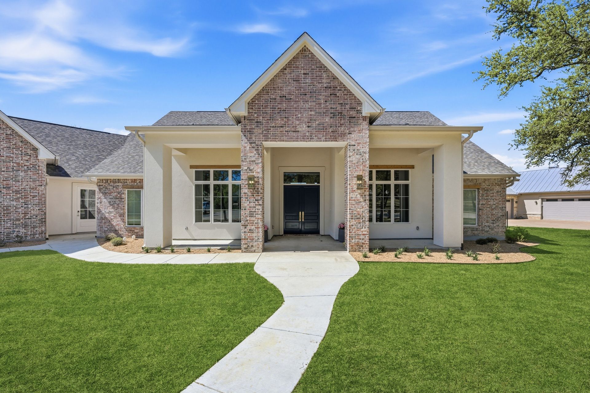 Single-story suburban house with a gabled entry, white columns, and a curved walkway across a green lawn