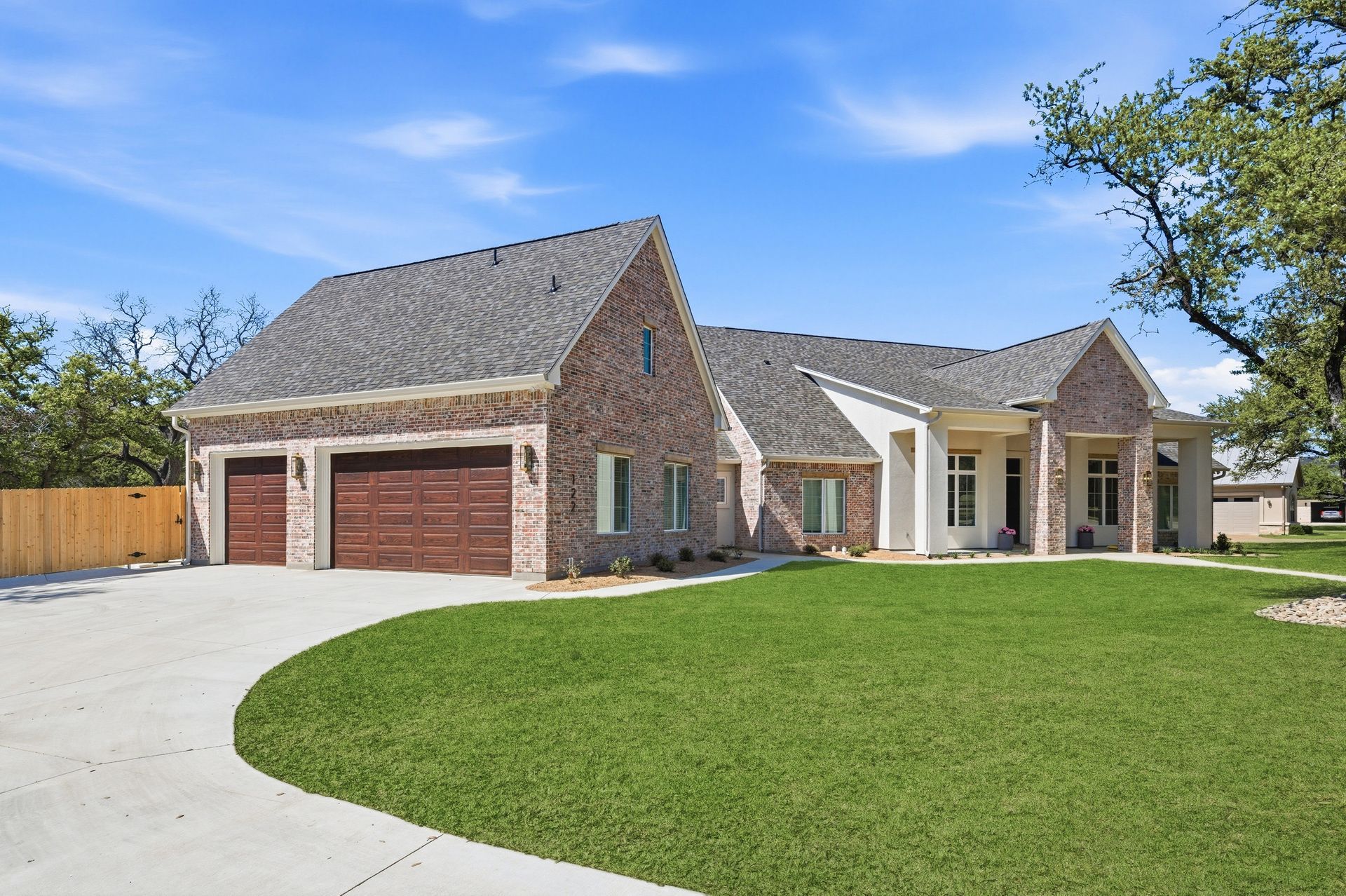 Brick suburban house with two-car garage, curved driveway, and green lawn under a blue sky
