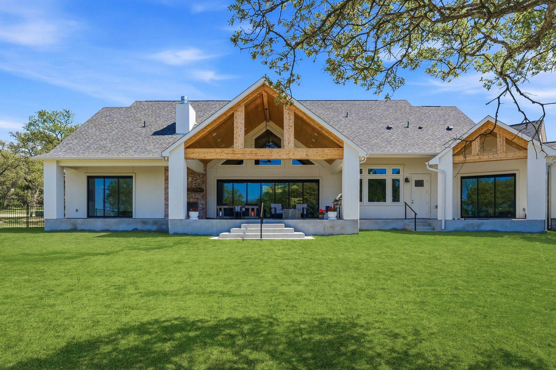 Modern house with large windows, wood-trimmed porch, and a wide green lawn under a clear blue sky
