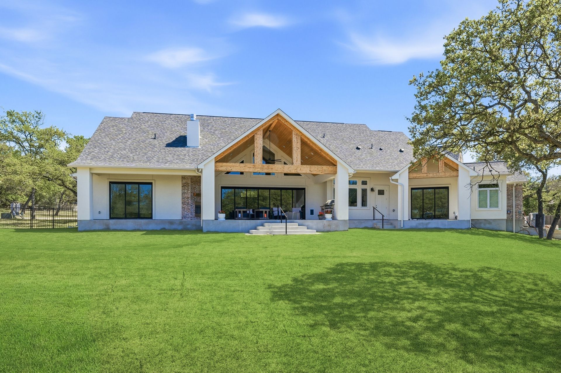 Modern single-story house with large covered patio and expansive green lawn under a blue sky