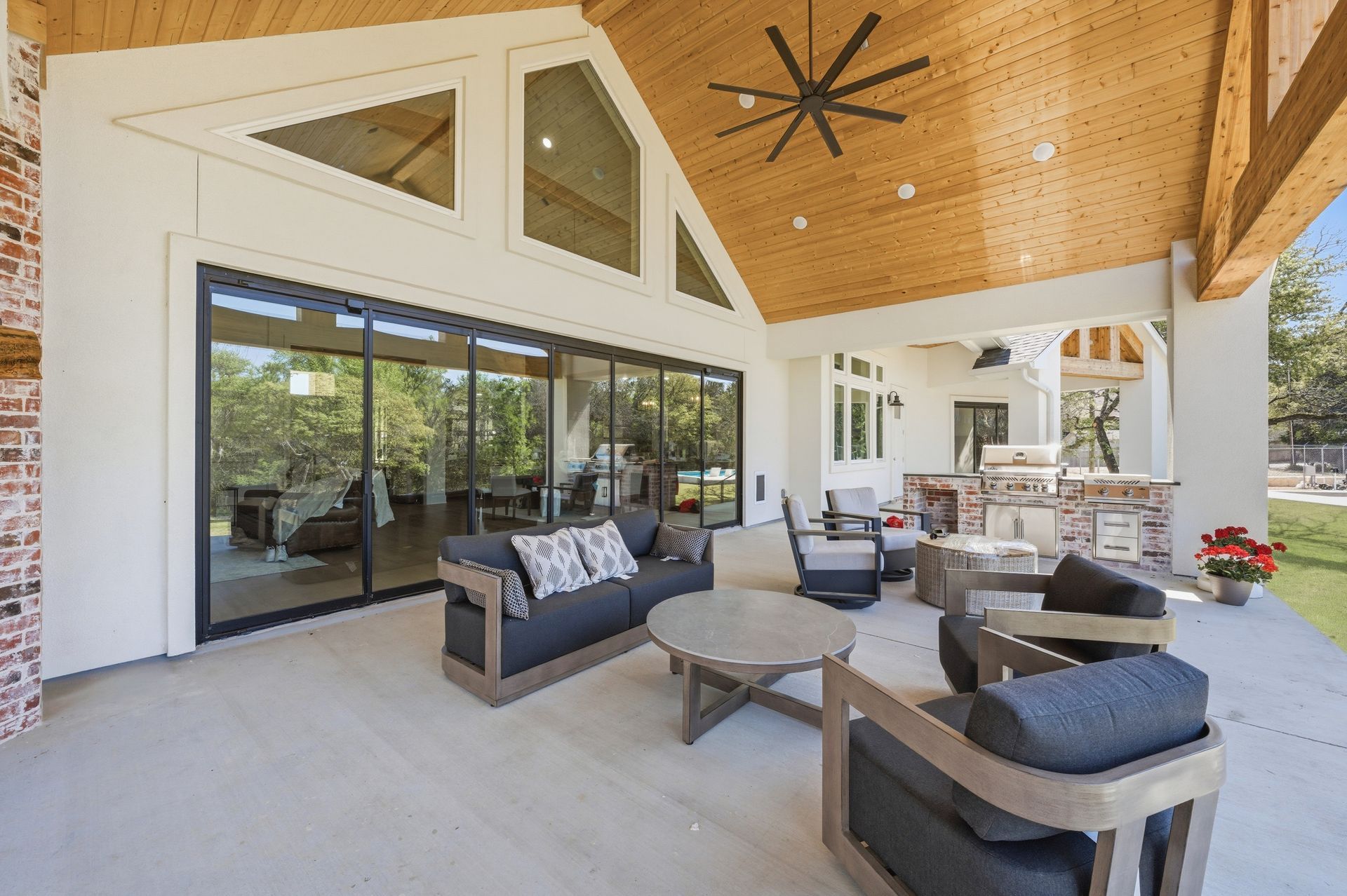Spacious covered patio with modern seating, large sliding glass doors, and a wood-paneled ceiling with a ceiling fan