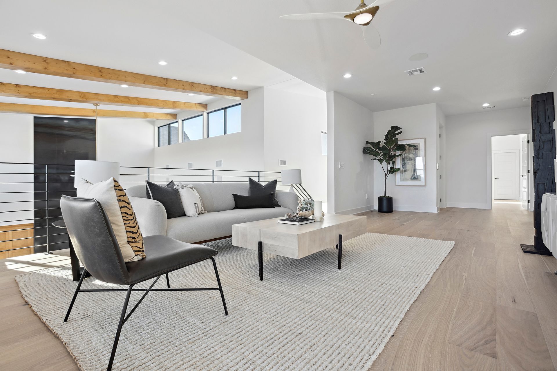 Bright open-plan living room with gray sofa, chair, coffee table, rug, wood accents, and kitchen in back