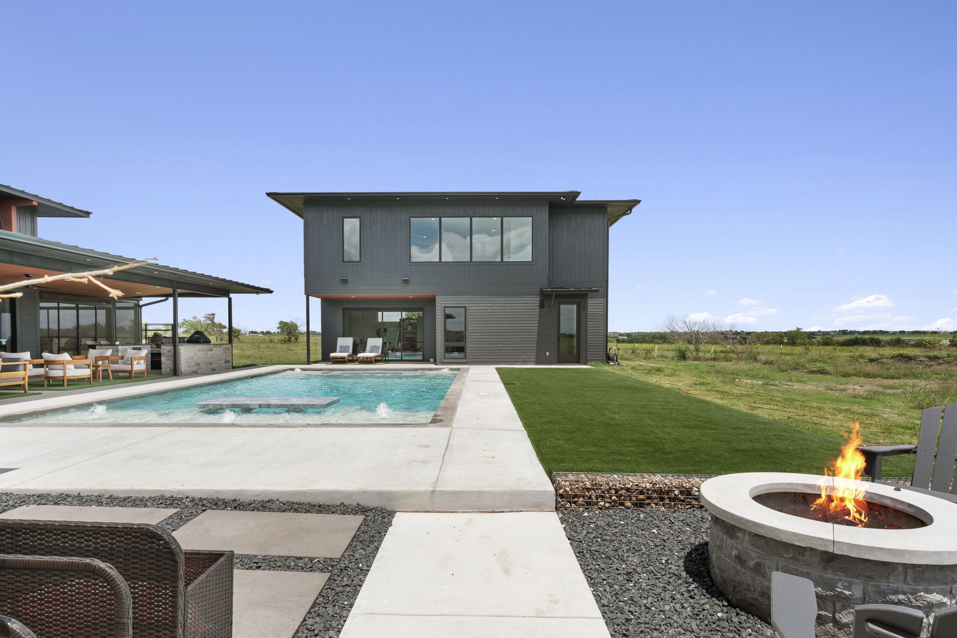 Modern backyard with a pool, patio, fire pit, and a two-story house under a clear sky