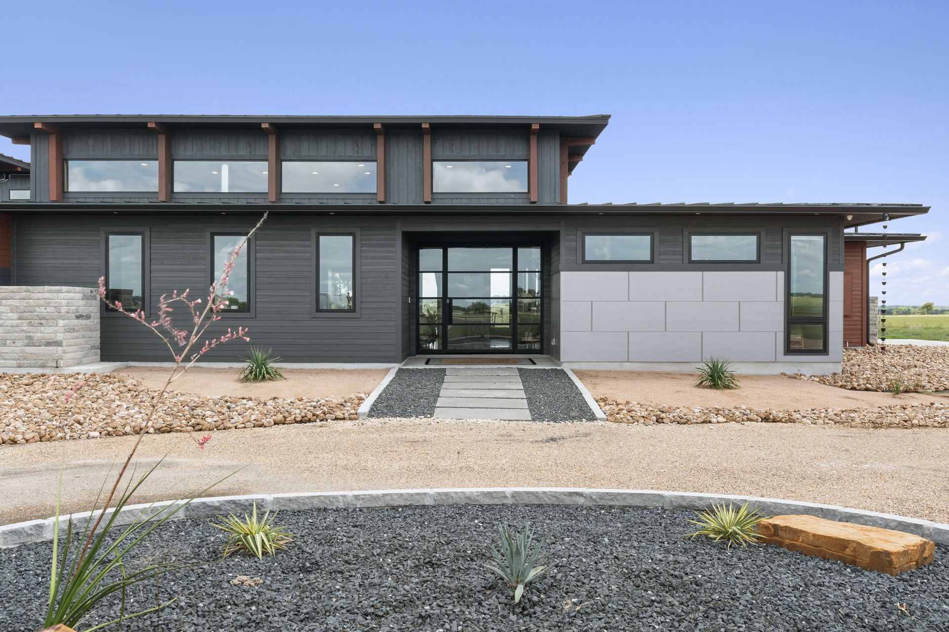 Modern dark-gray house exterior with large windows, a gravel front yard, and a double garage