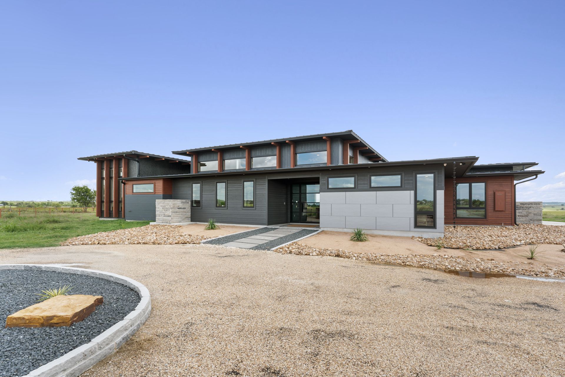 Modern flat-roof house with large windows and gravel driveway under a clear sky