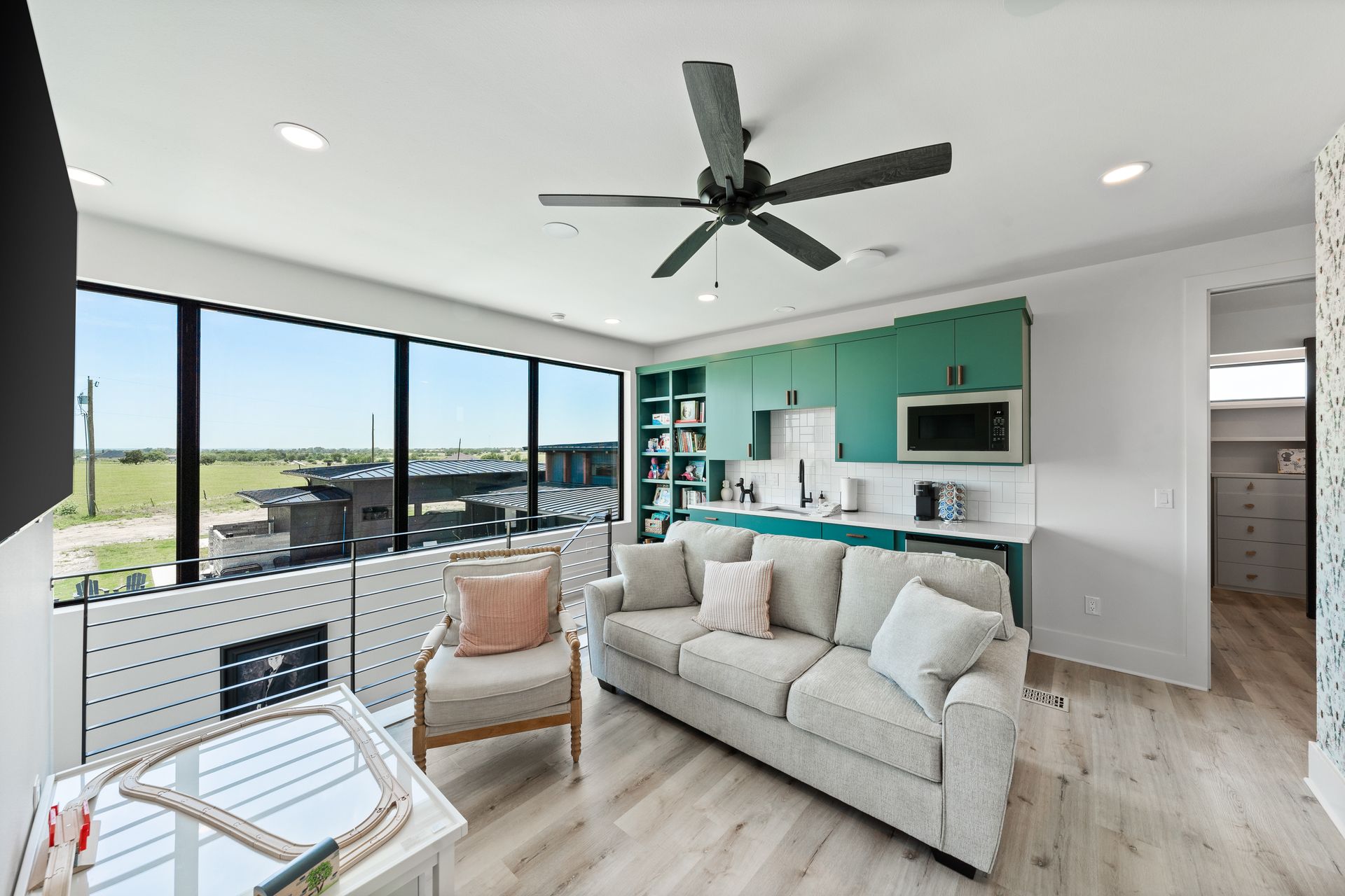 Bright modern living room with teal accent wall, white sofa, ceiling fan, and large windows overlooking water.