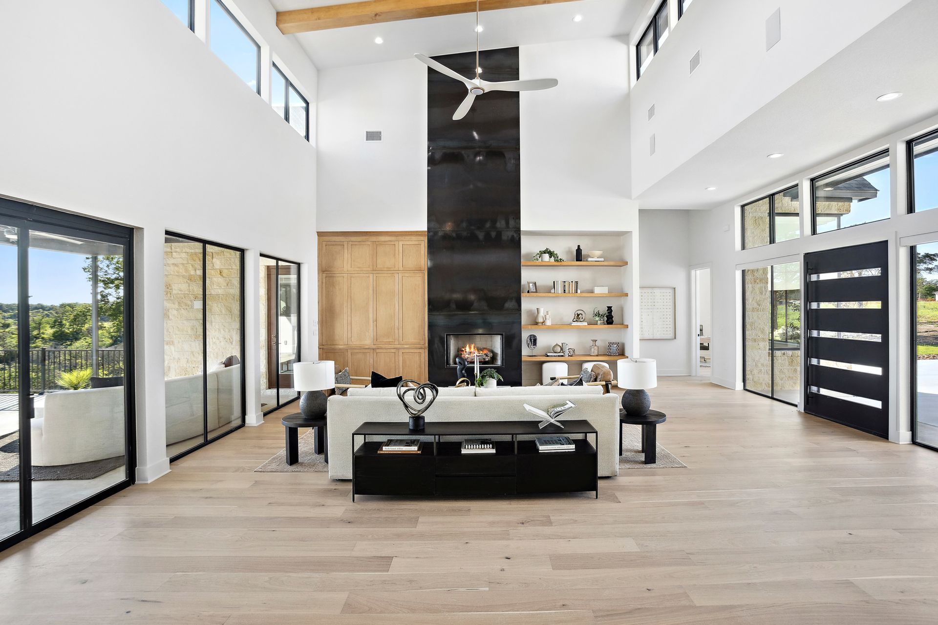 Modern open-concept living room with fireplace, large windows, and black-and-white furnishings