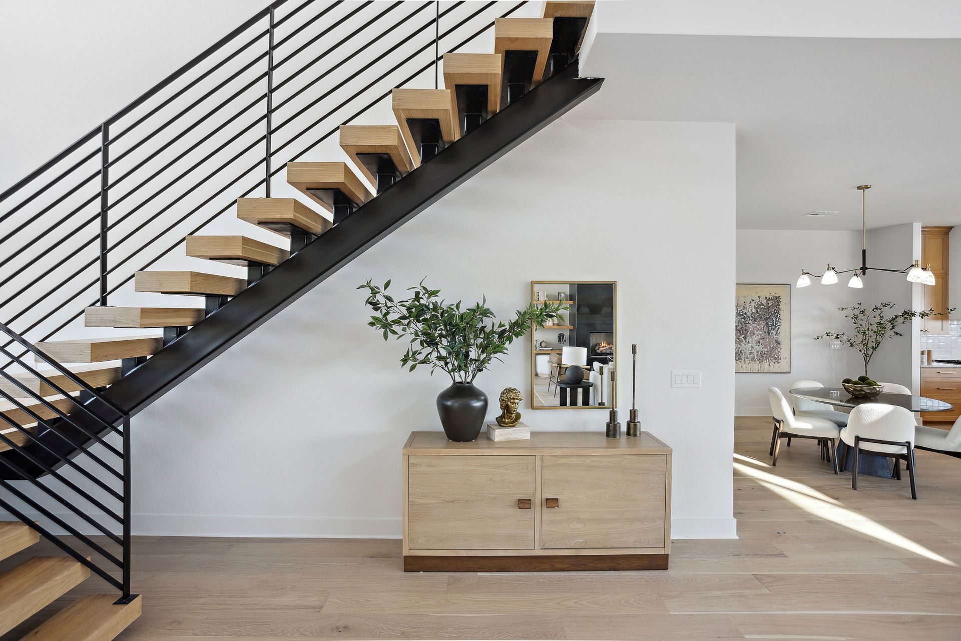 Modern home interior with floating staircase, wooden cabinet, and open dining area