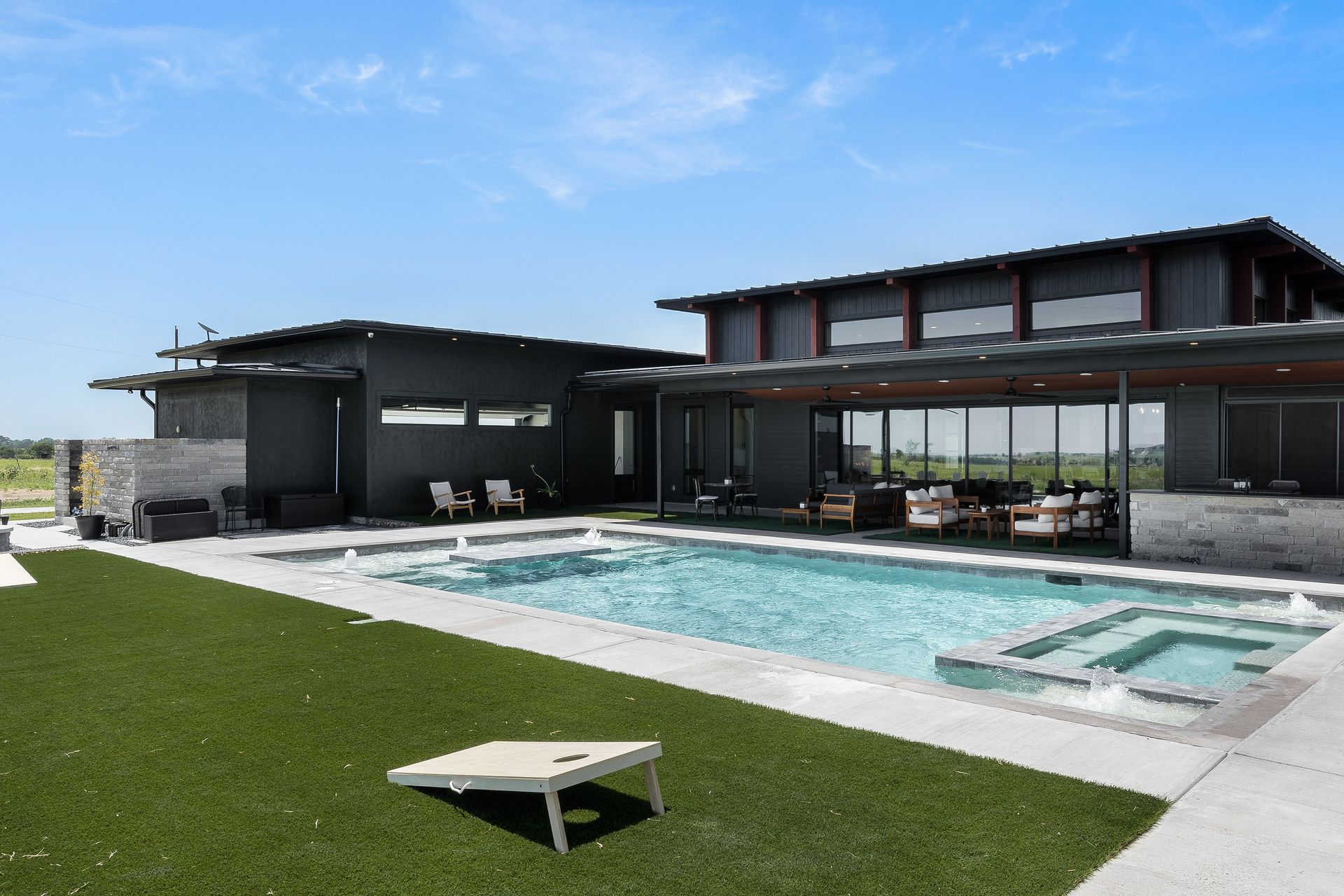 Modern house with a backyard pool, patio seating, and green lawn under a clear sky