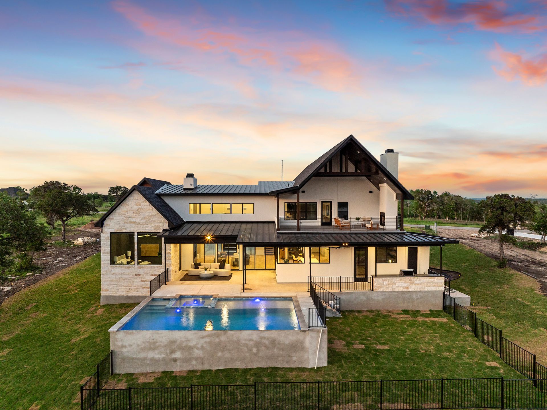 Modern two-story house with a lit pool and sunset sky in a grassy rural setting