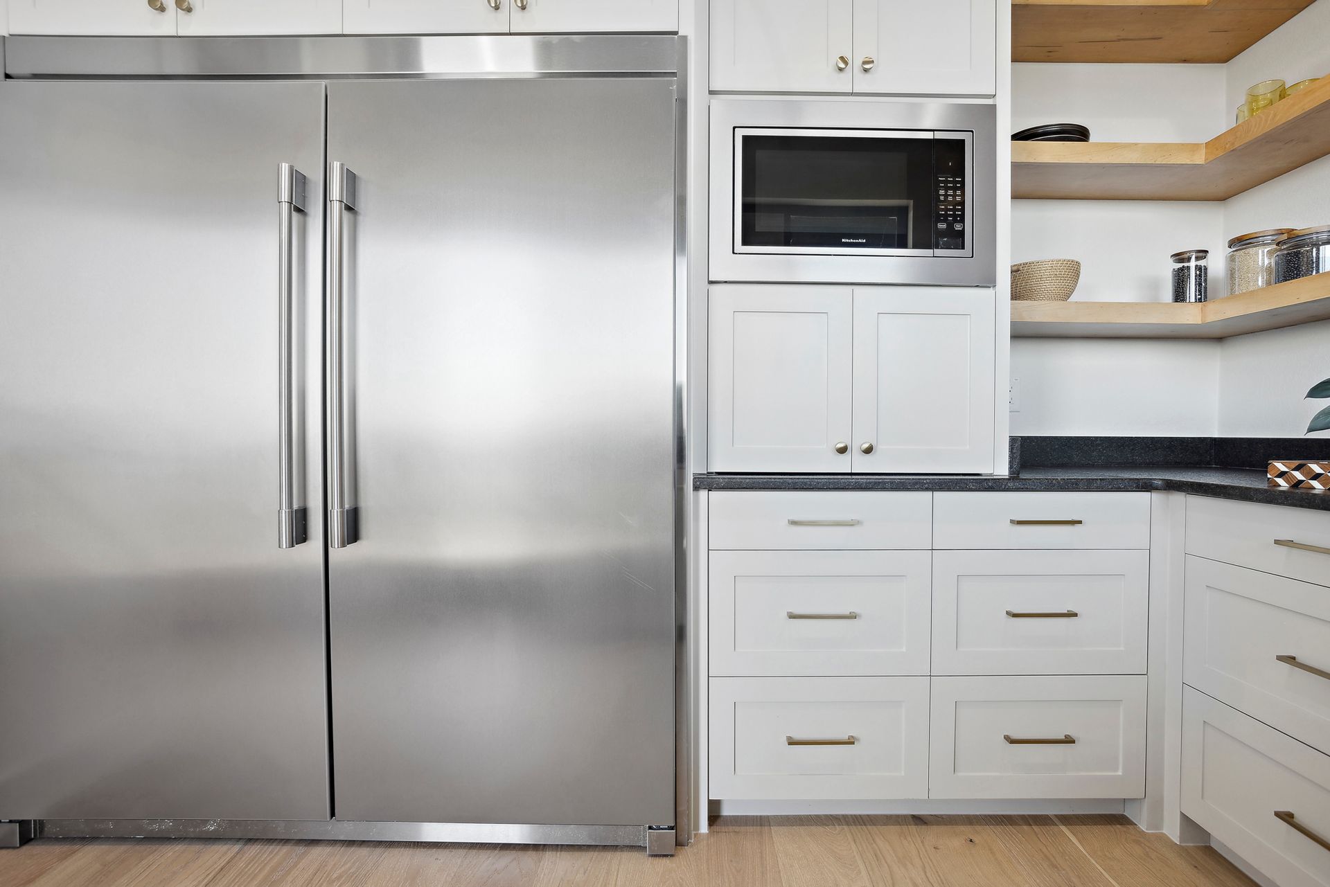Modern kitchen with stainless steel refrigerator, microwave, white cabinets, and granite countertops